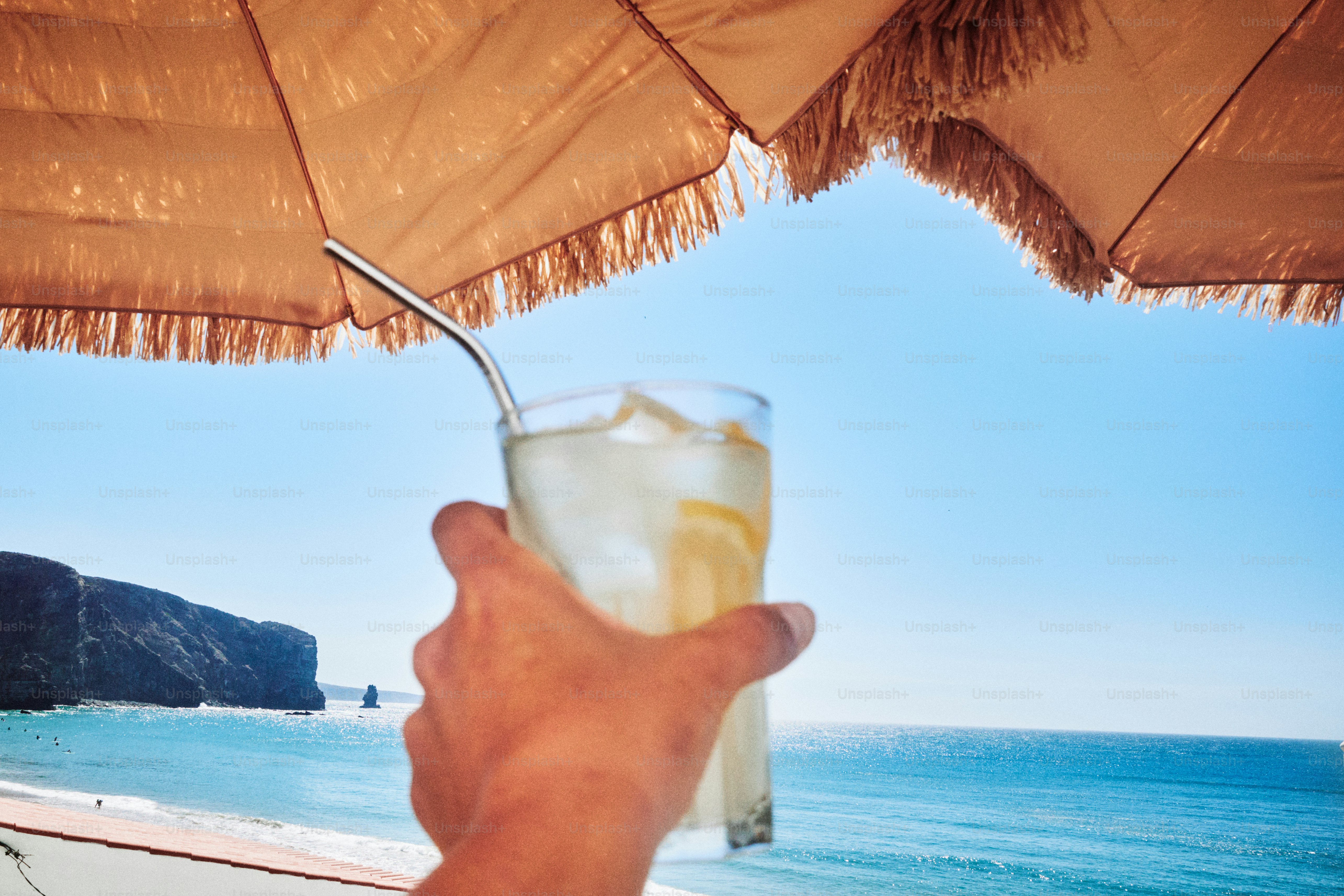 Con la mano sosteniendo una bebida refrescante junto al mar.