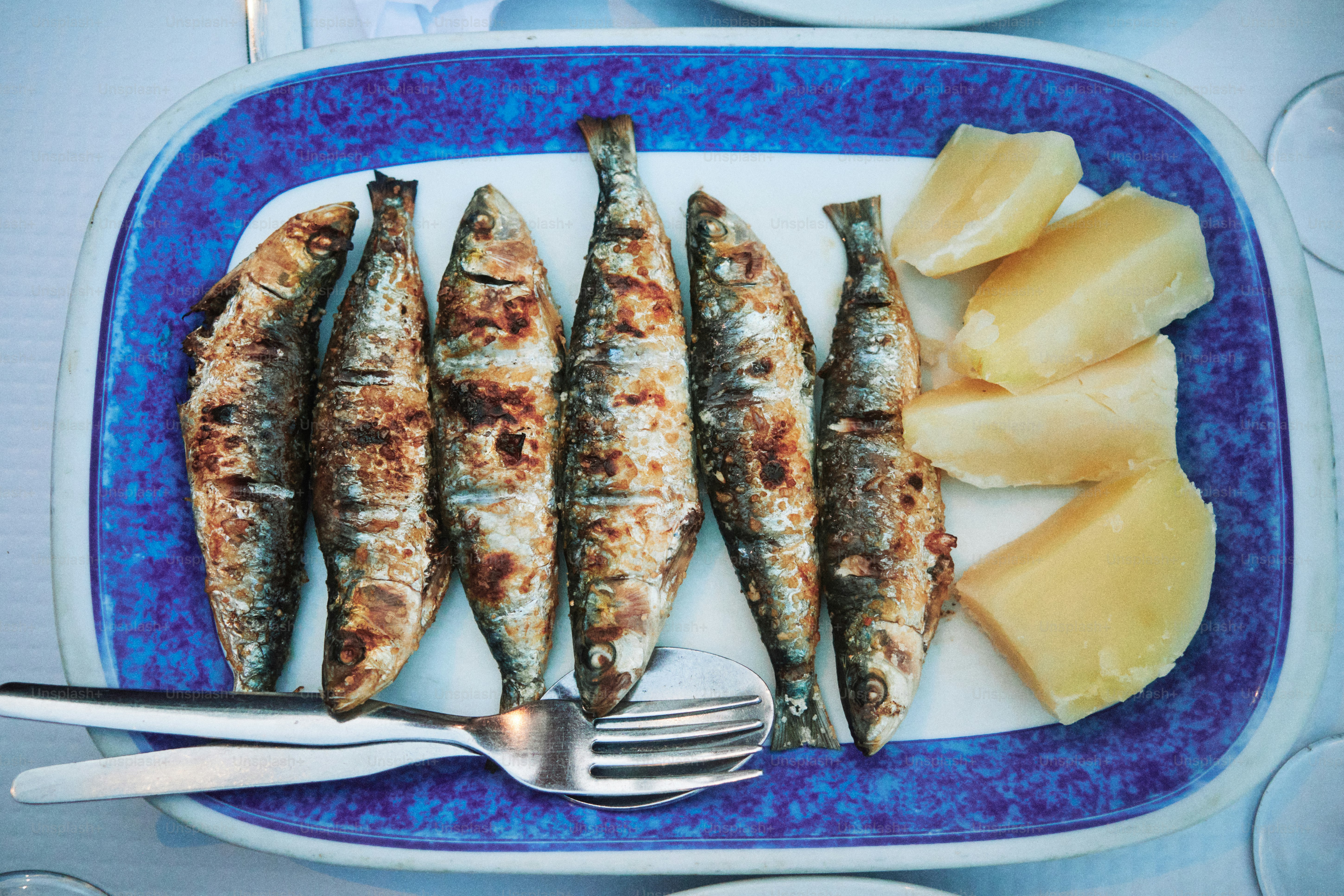 Grilled sardines with potatoes on a blue plate