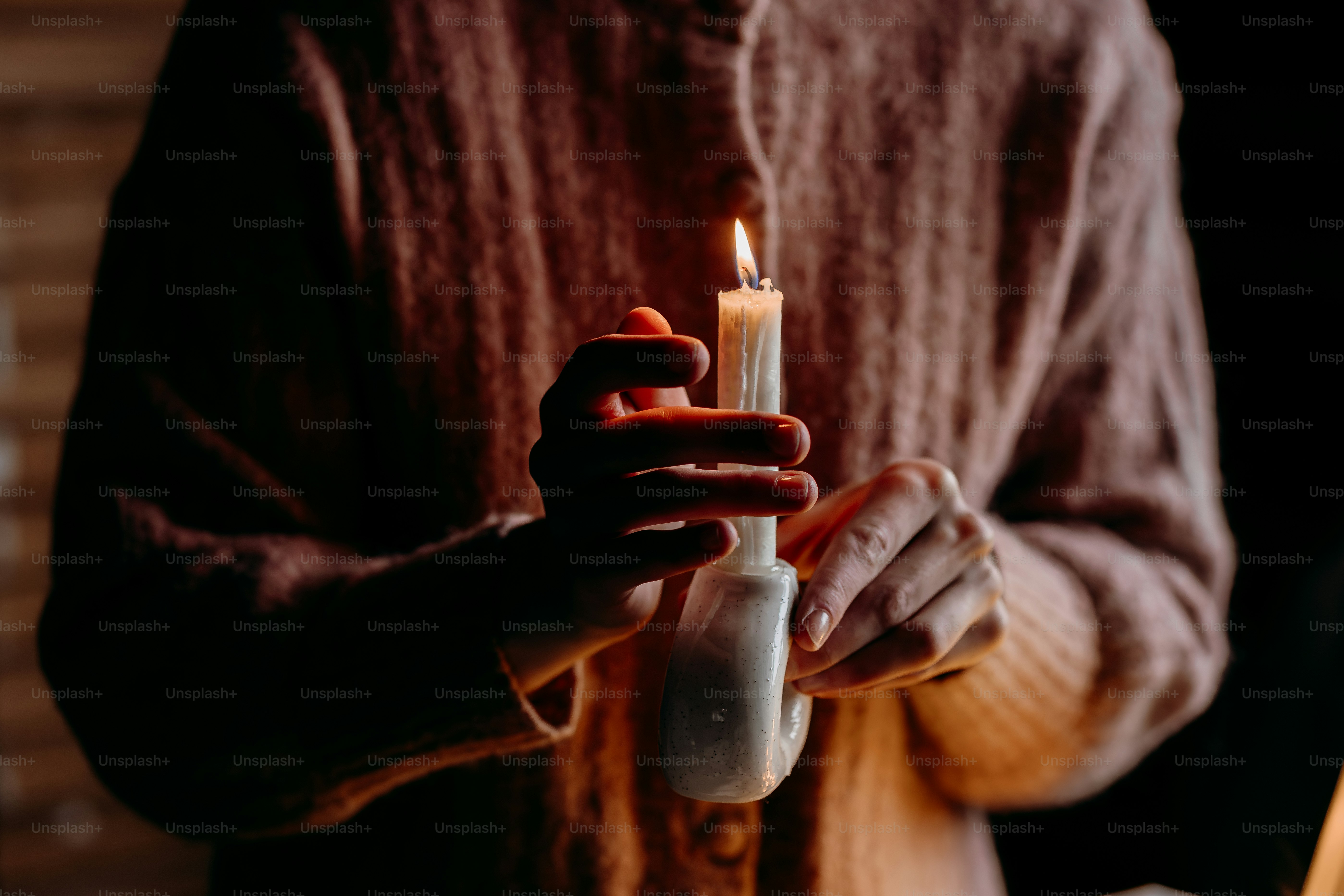 Person holding a lit candle in the dark.