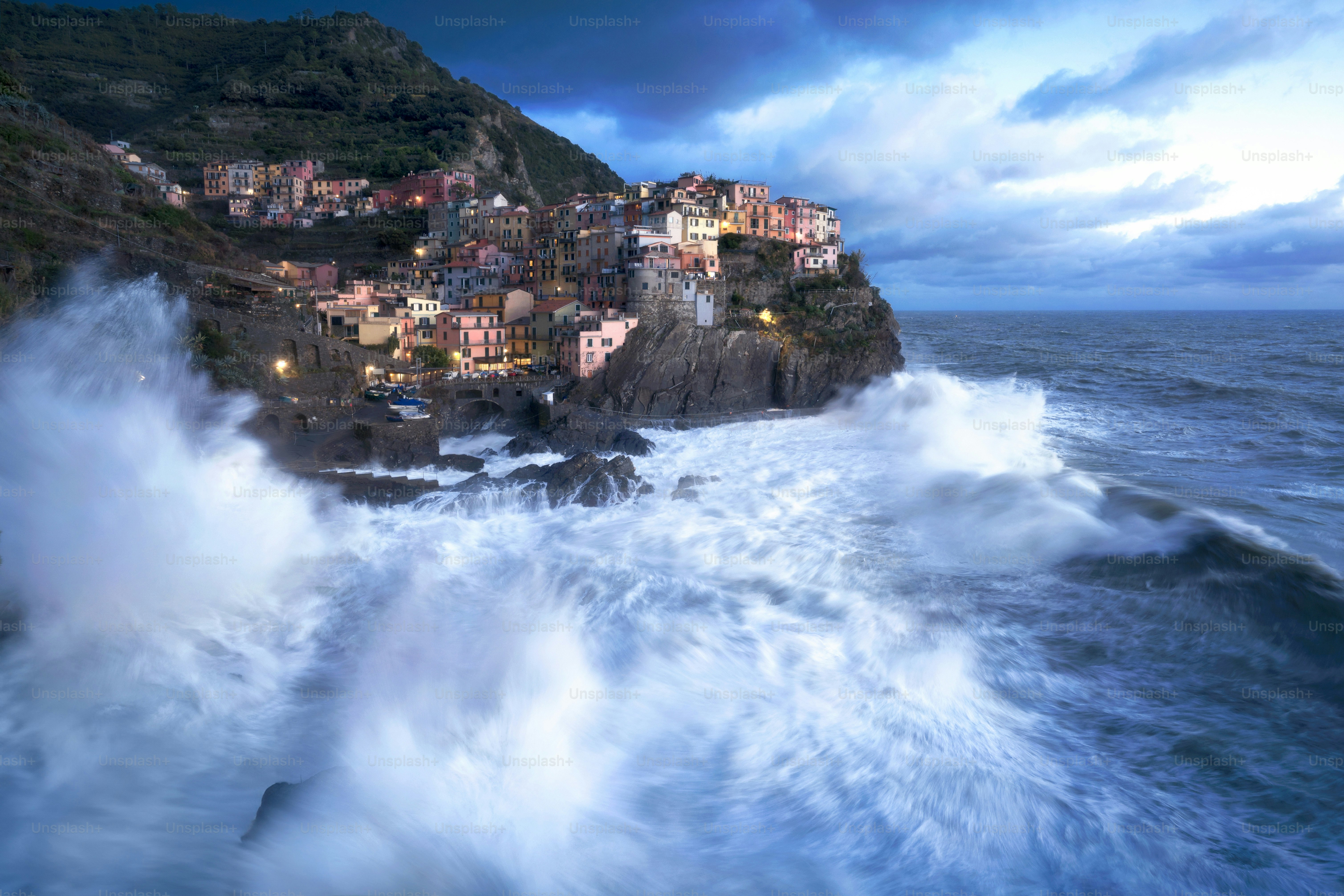 Waves crash against a cliffside village at dusk.