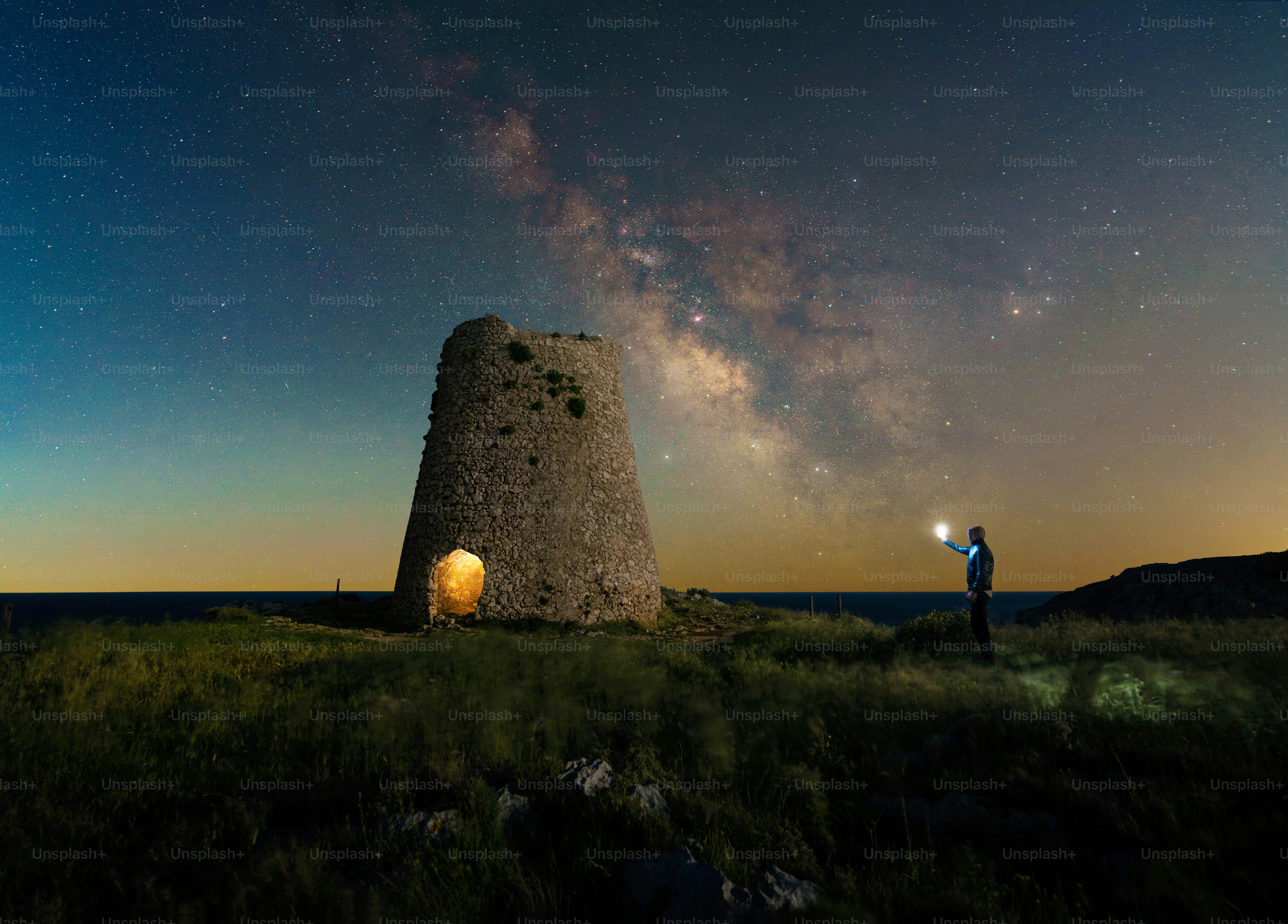Stone tower under the milky way with person holding light.