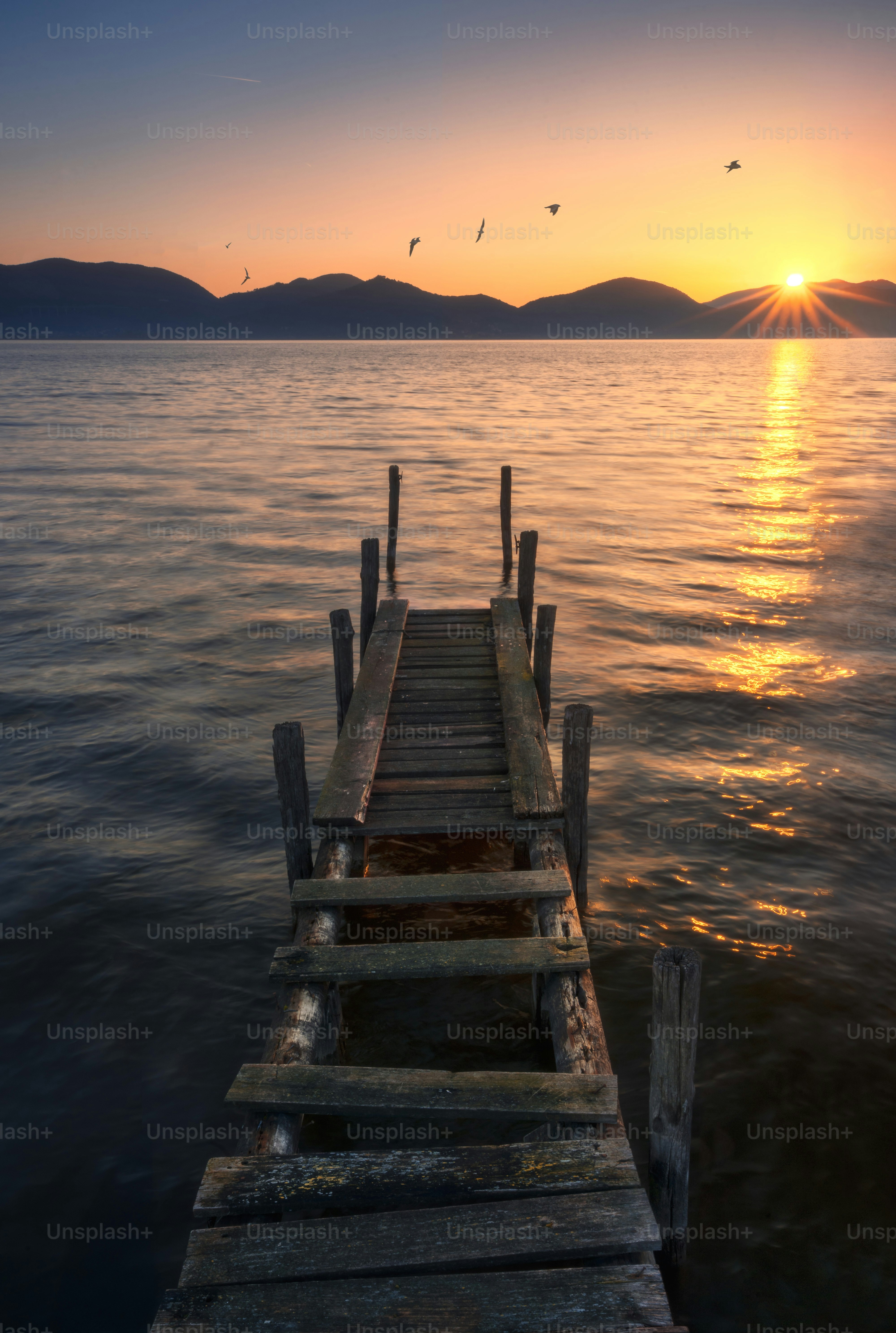 Wooden pier on a lake at sunset with mountains.
