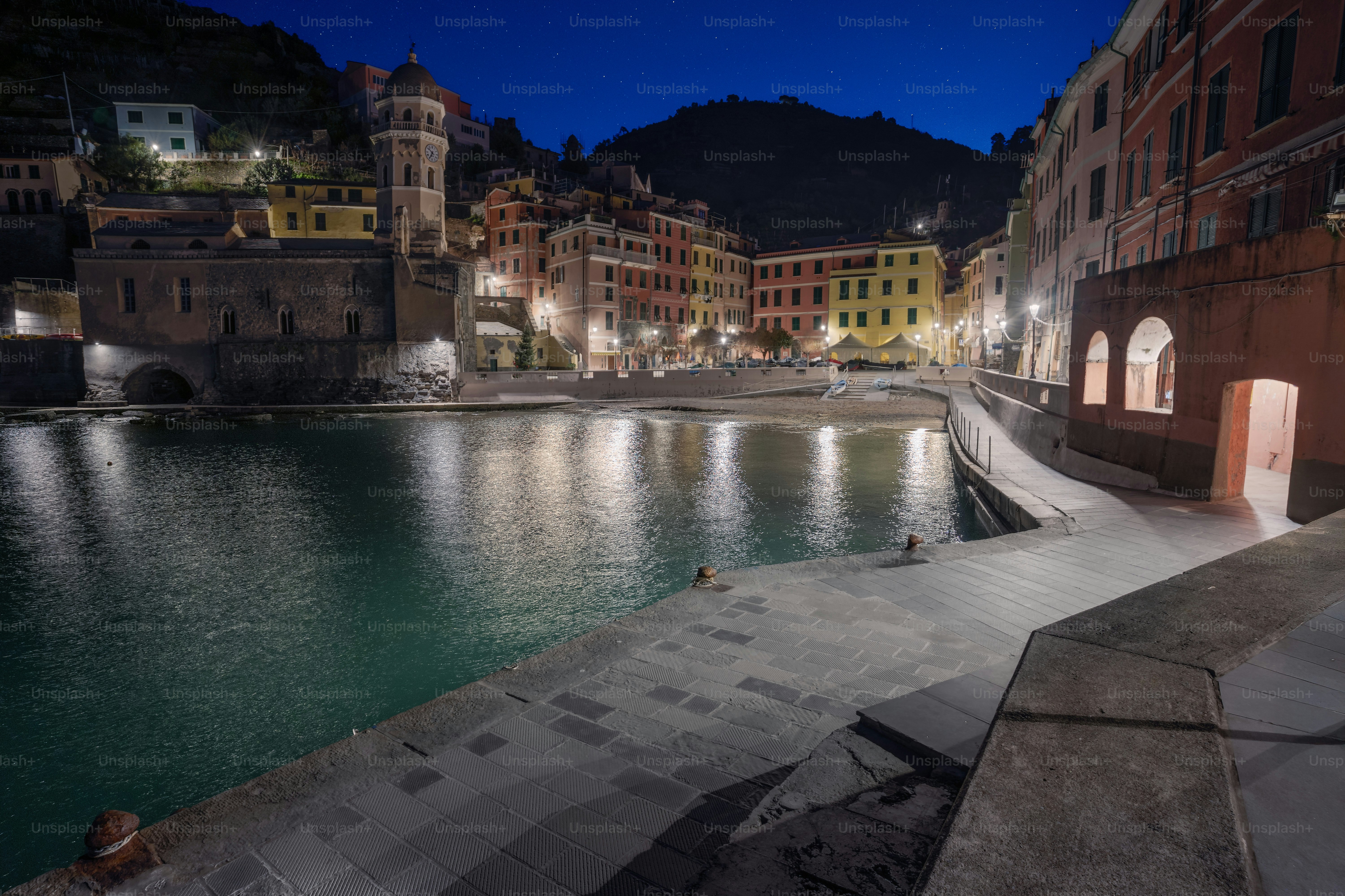Coastal village illuminated at night with reflections on water.