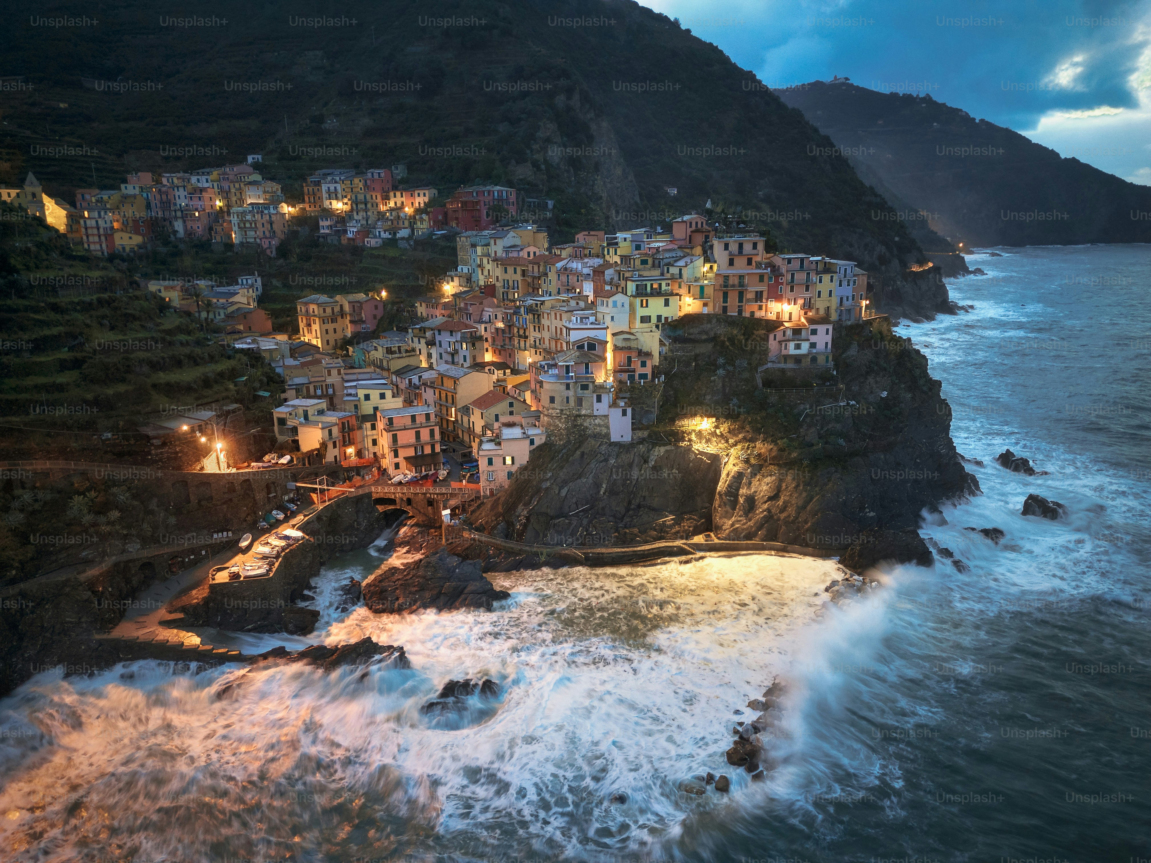 Coastal village lights up at dusk with crashing waves.