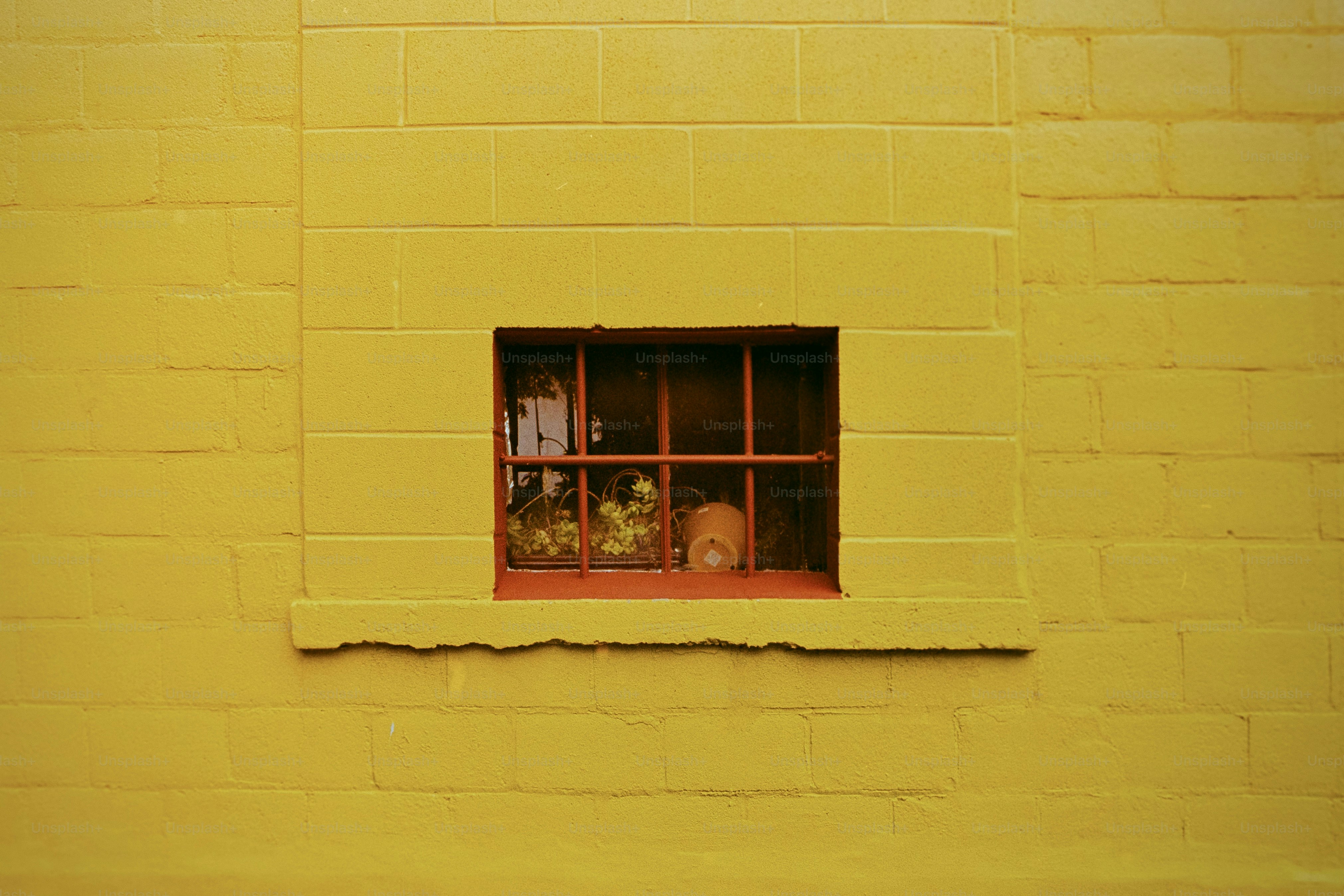 Une petite fenêtre encastrée dans un mur de briques jaune vif.