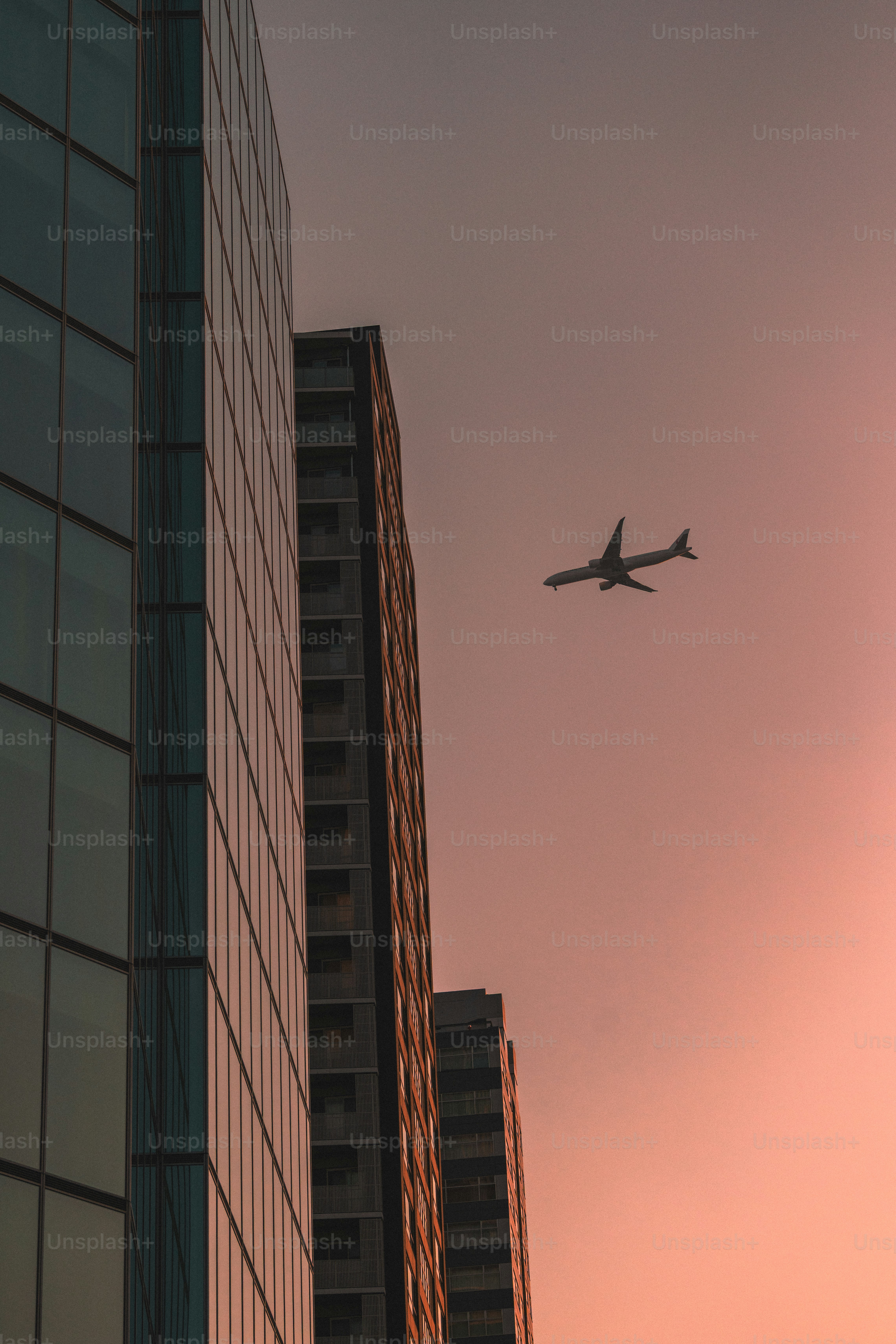 Airplane flying past modern buildings at sunset