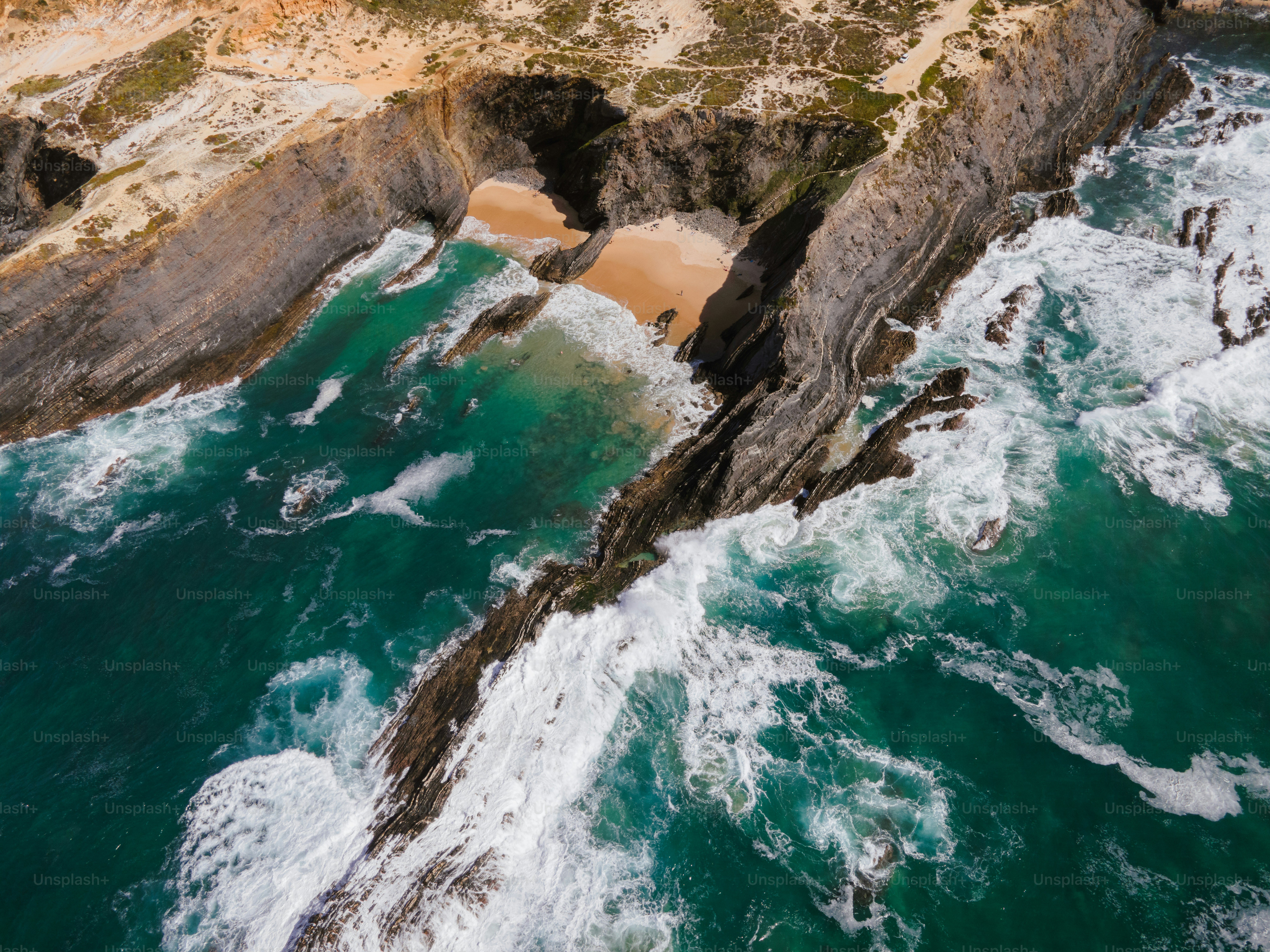Waves crash against rocky coastline with sandy cove.