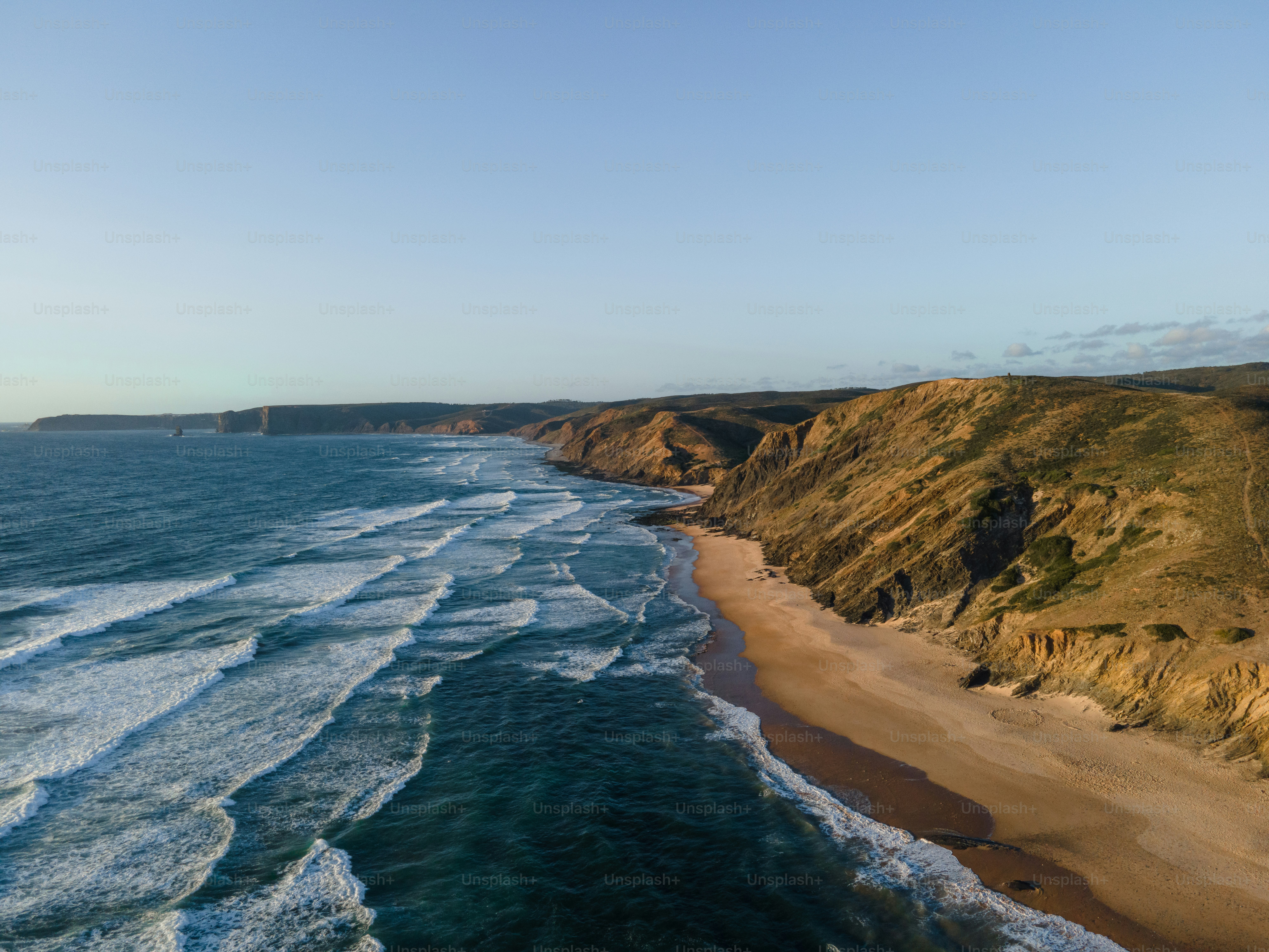 Waves crash on a sandy beach along rugged cliffs.