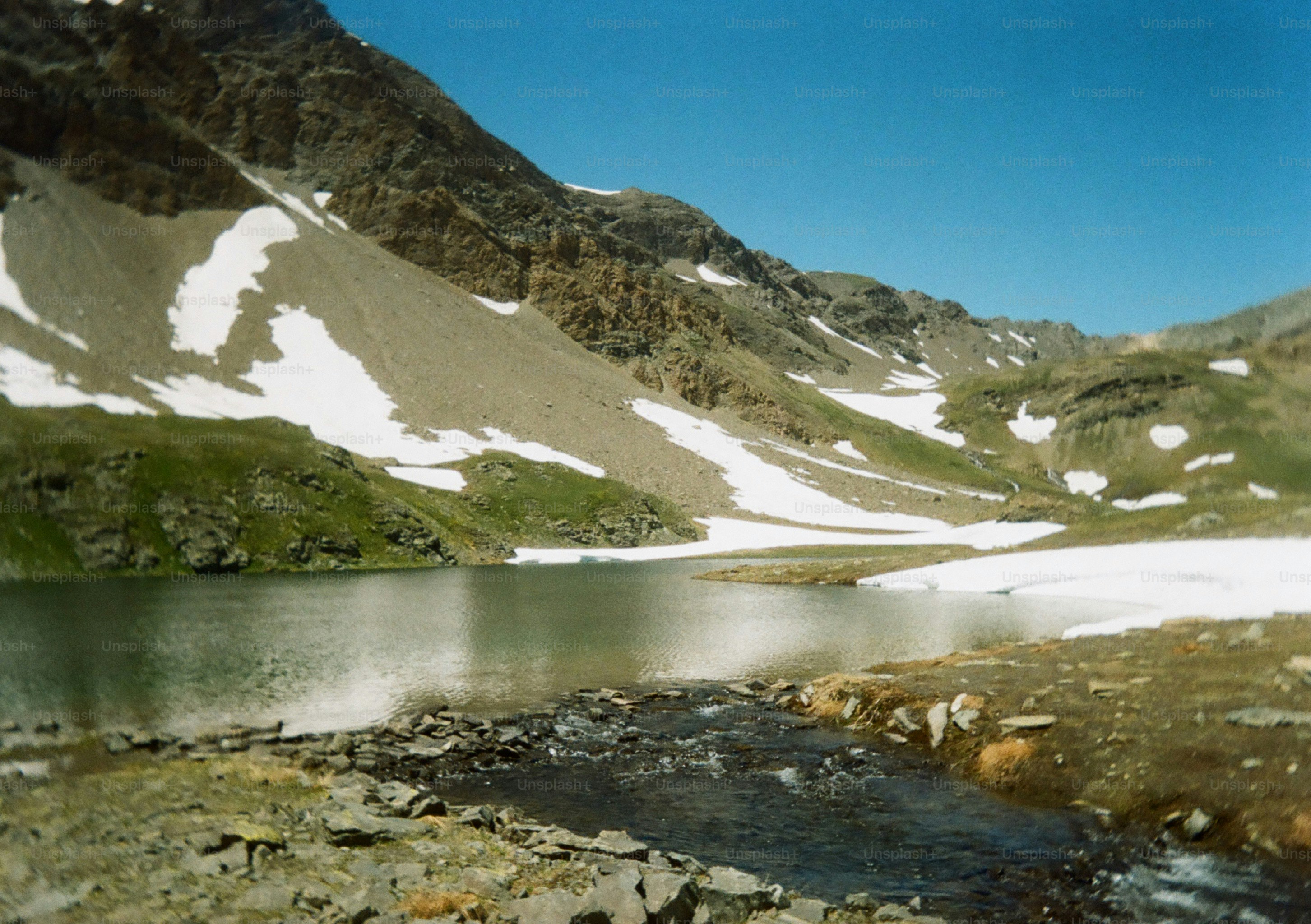 Lago de montaña con parches de nieve y arroyo