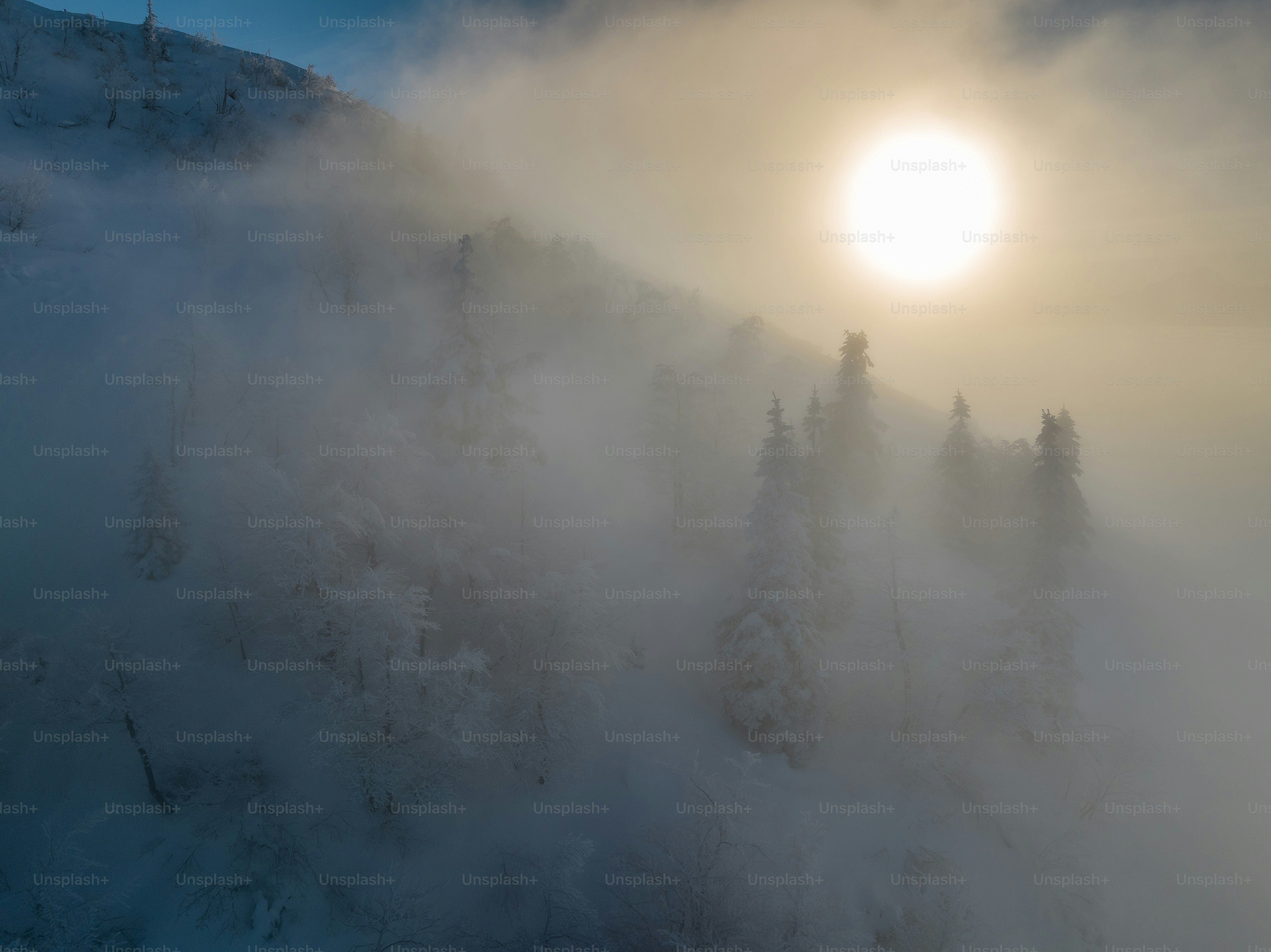 Sunlight shines through fog on a snowy mountain.
