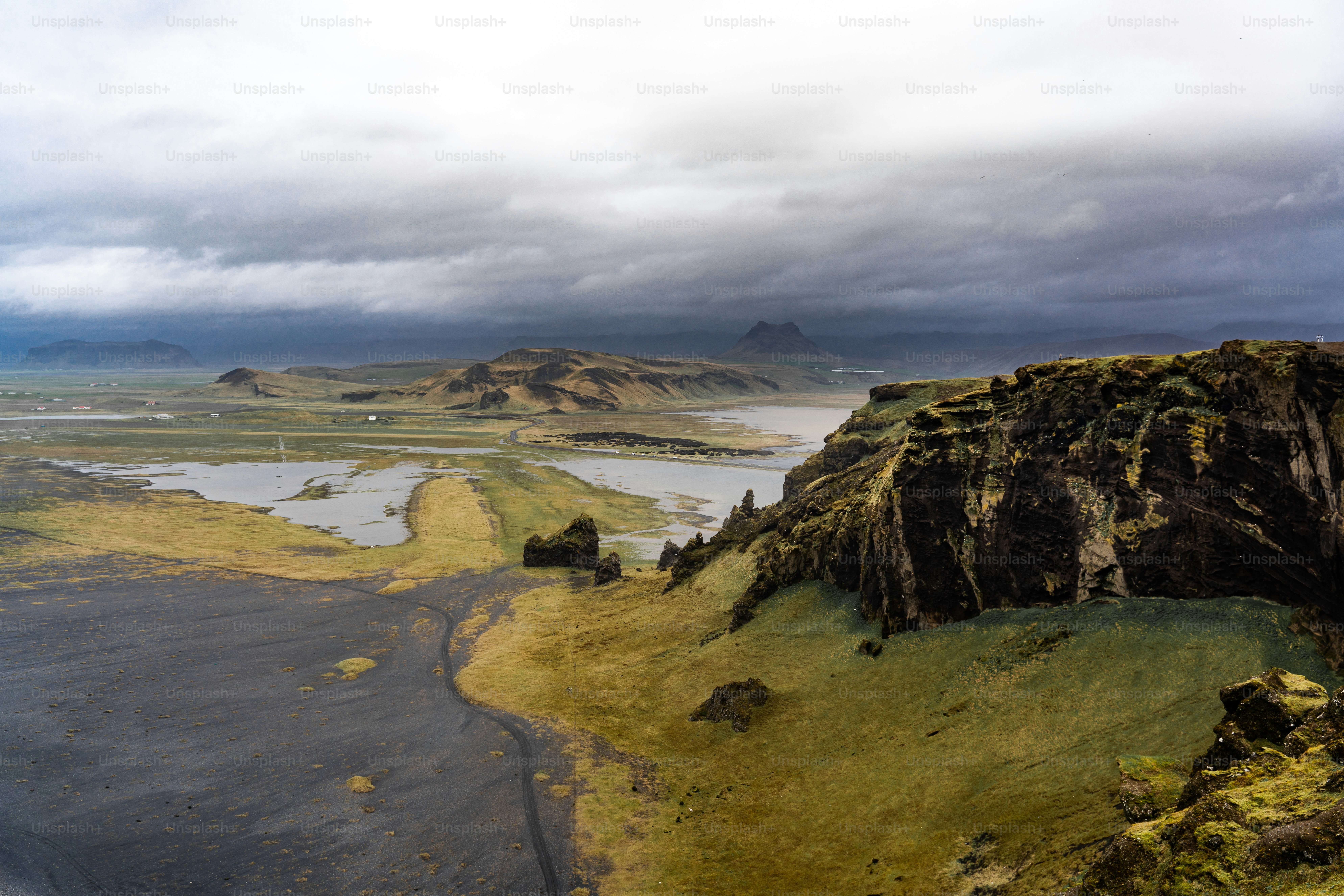 Rugged cliffs overlook a vast, moody landscape under stormy skies.