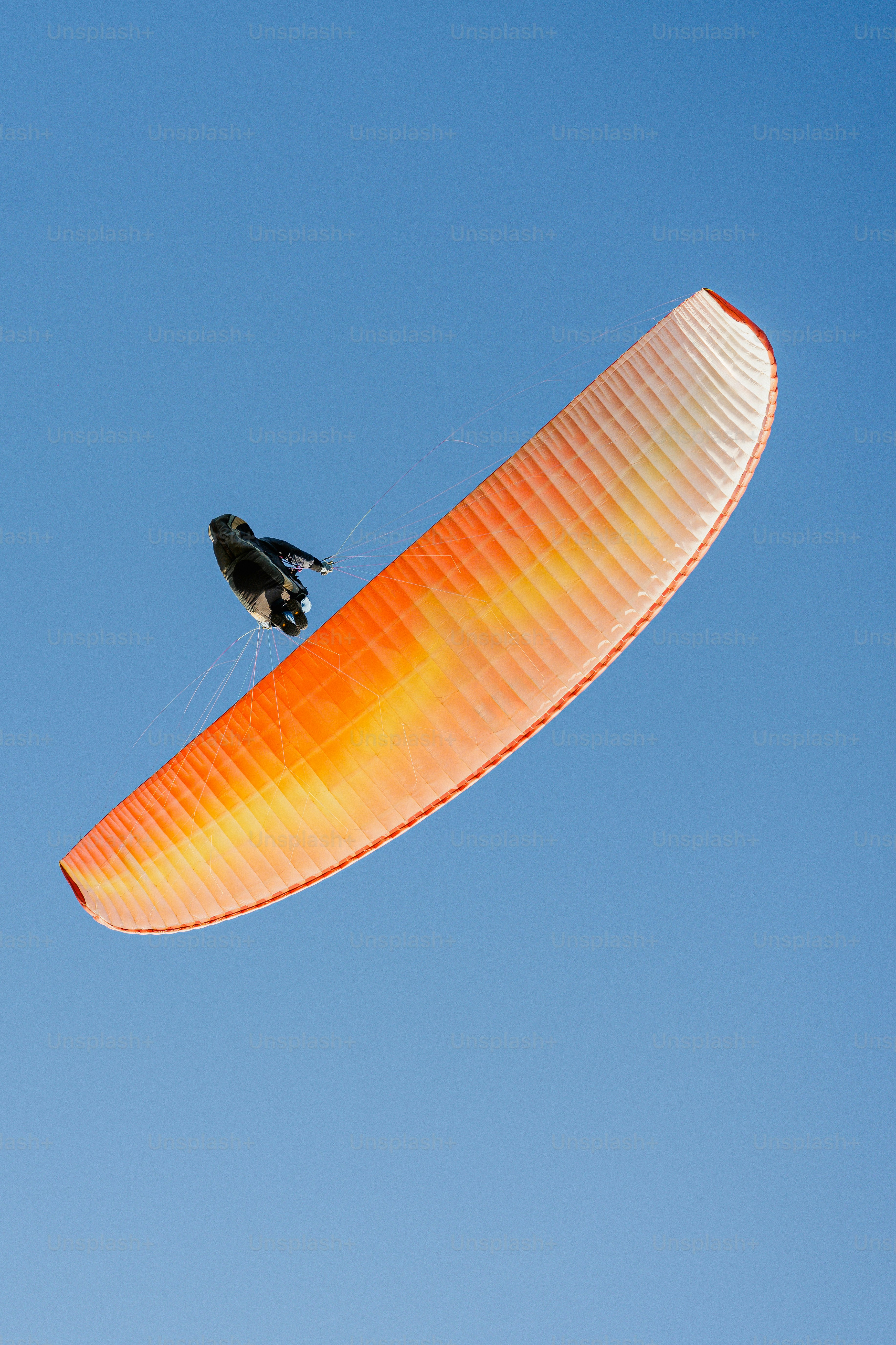 A paraglider soars against a clear blue sky.