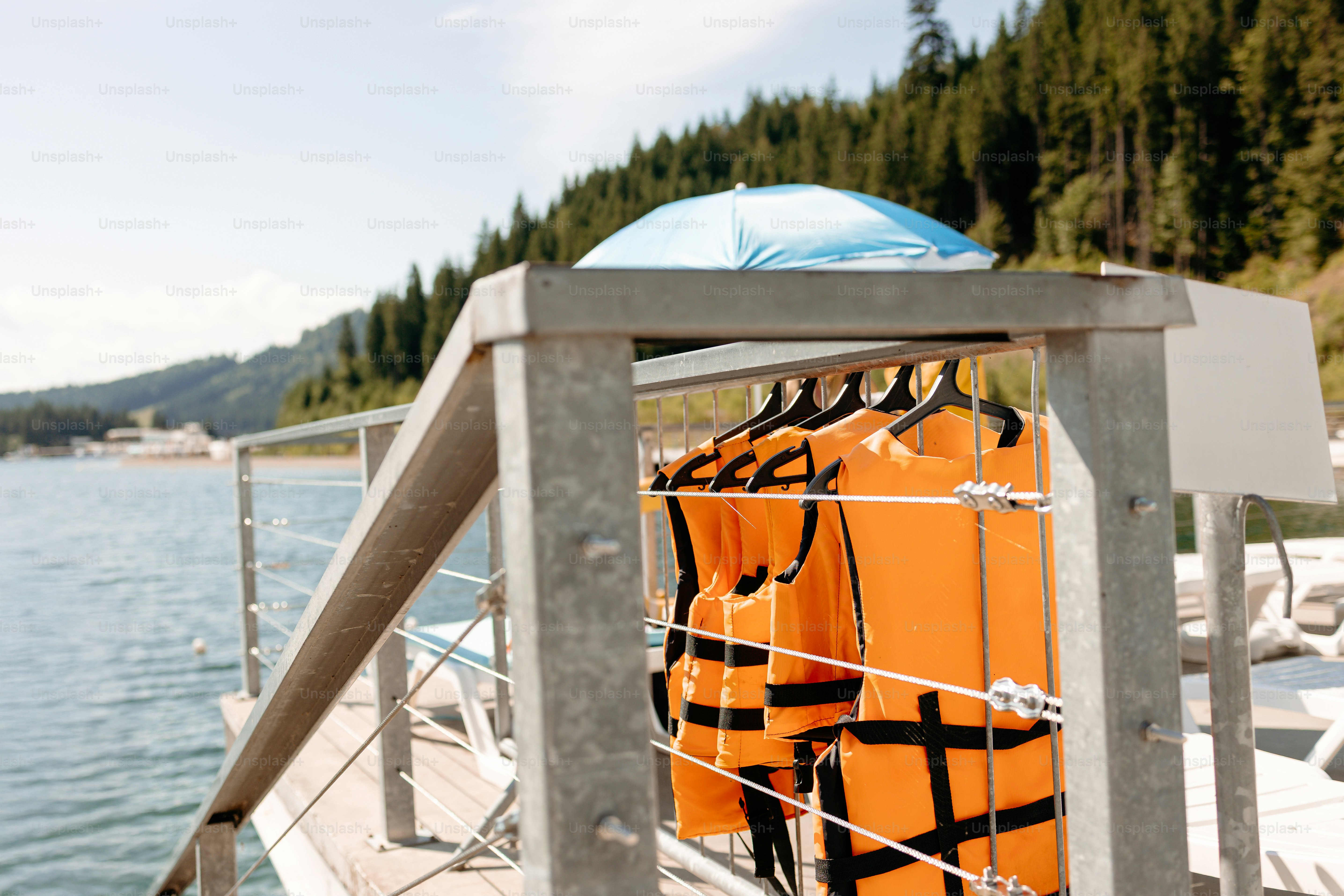 Orange life vests hanging on a railing by a lake
