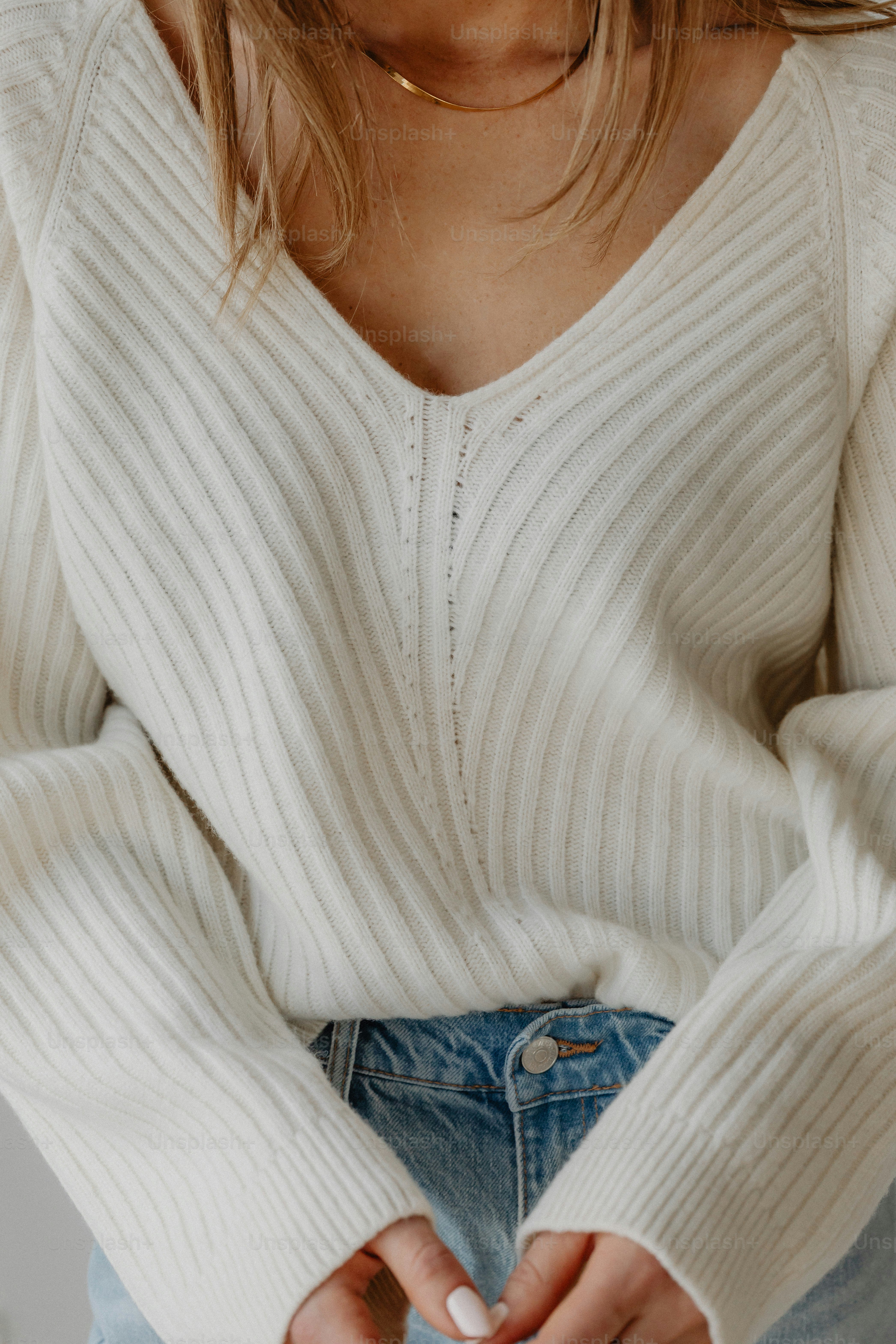 Woman wearing a cream ribbed v-neck sweater and jeans.