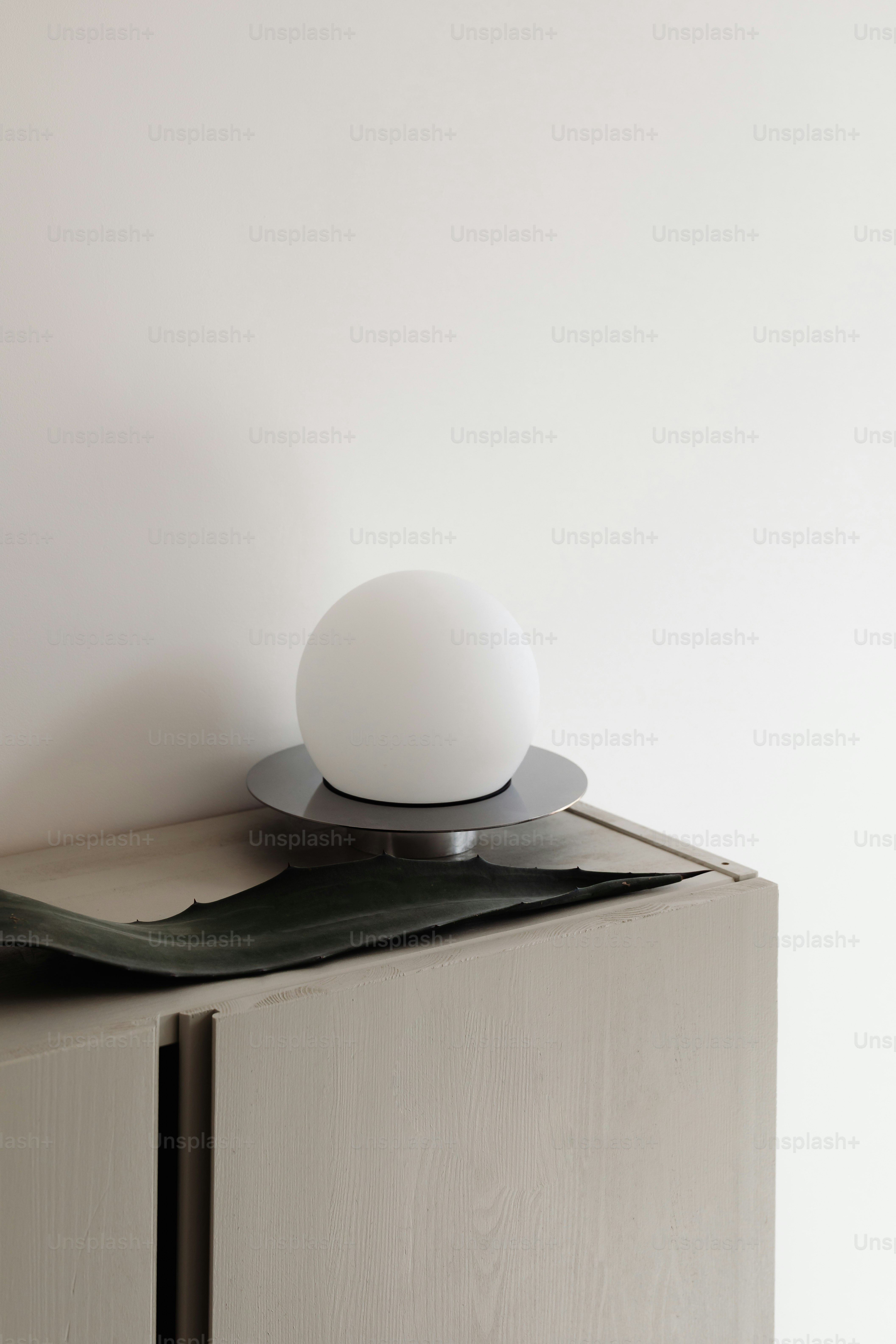 Une lampe minimaliste sur un meuble avec une feuille.