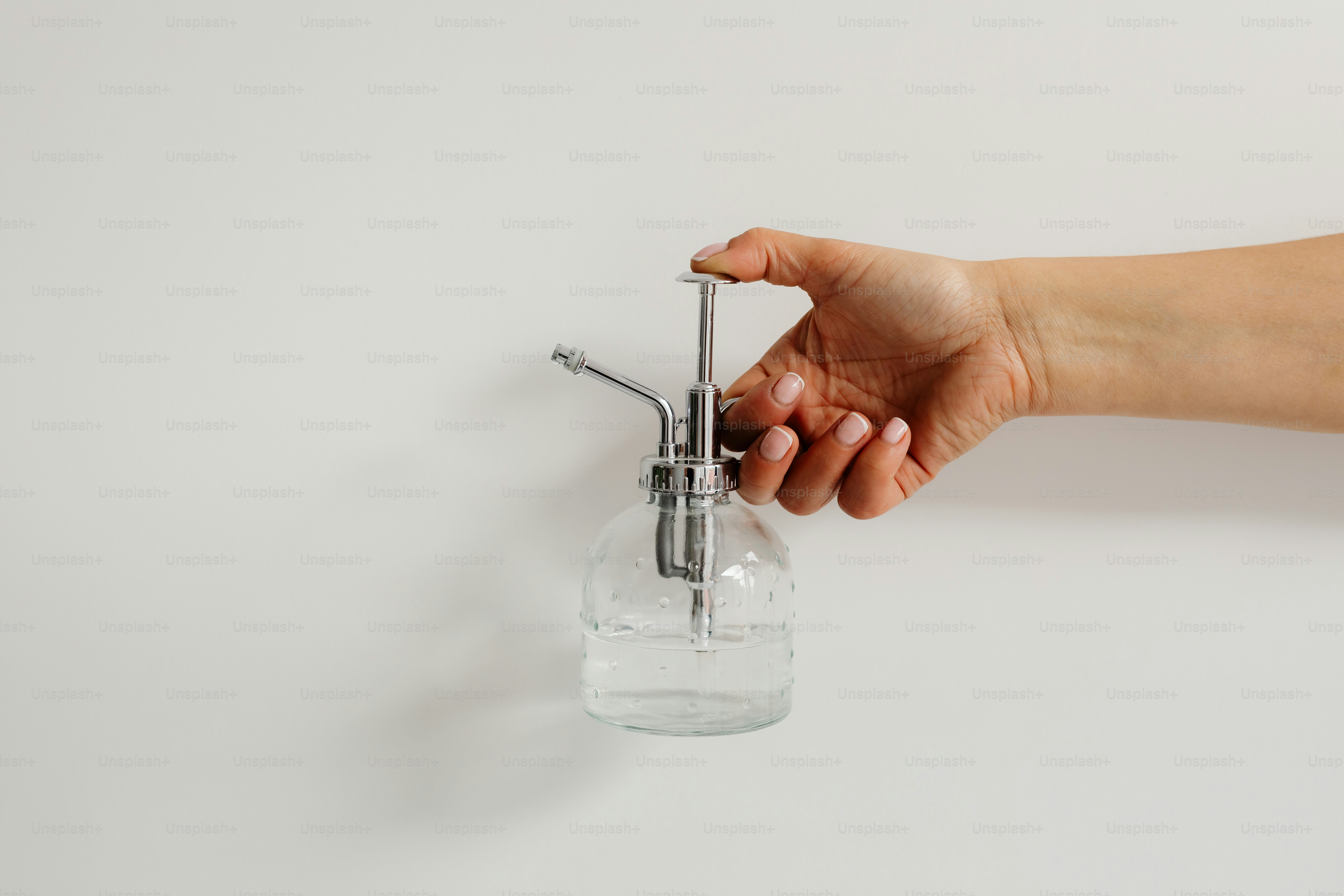 Hand hält eine Glassprühflasche mit Wasser.