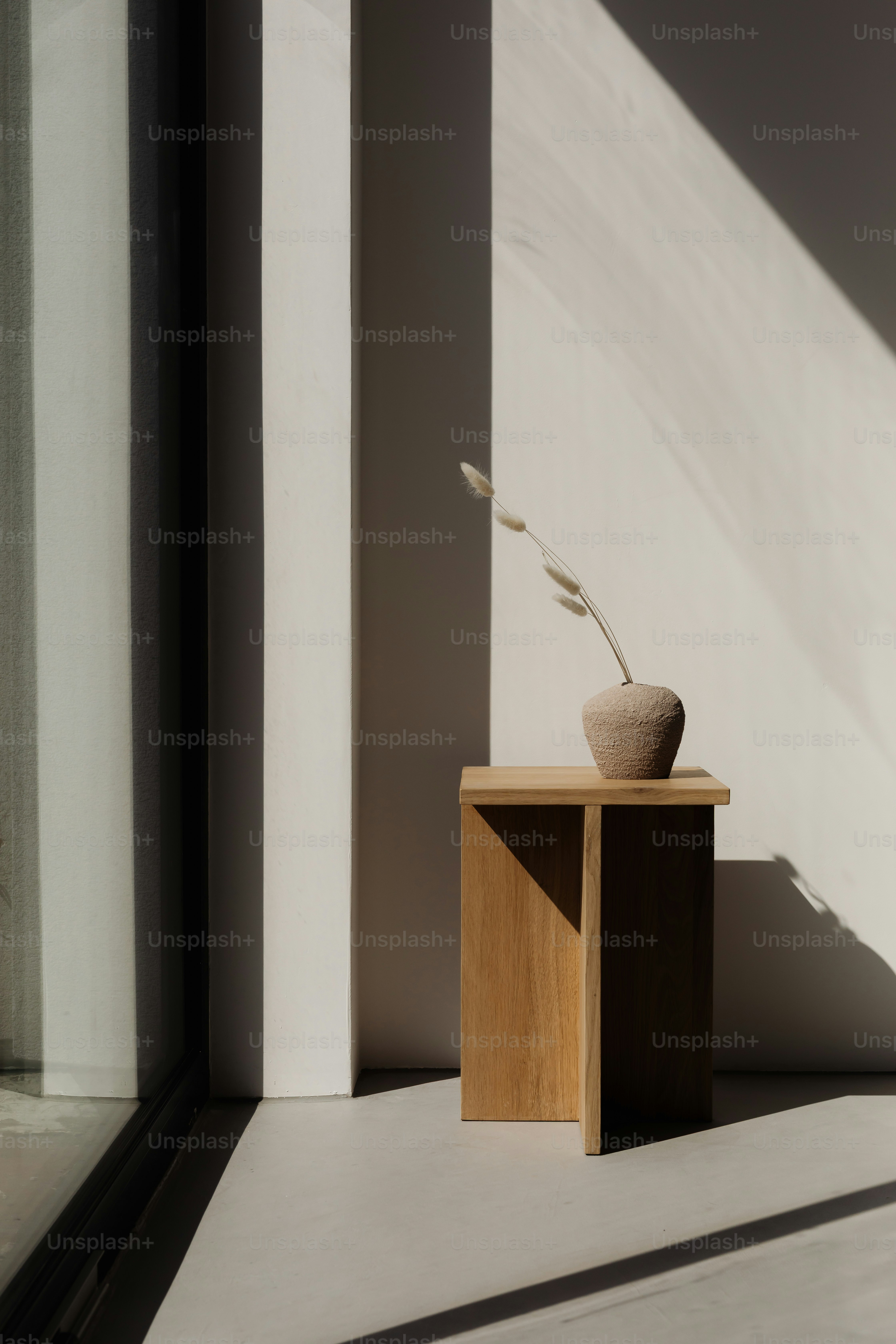 A vase with dried grass on a wooden stool.