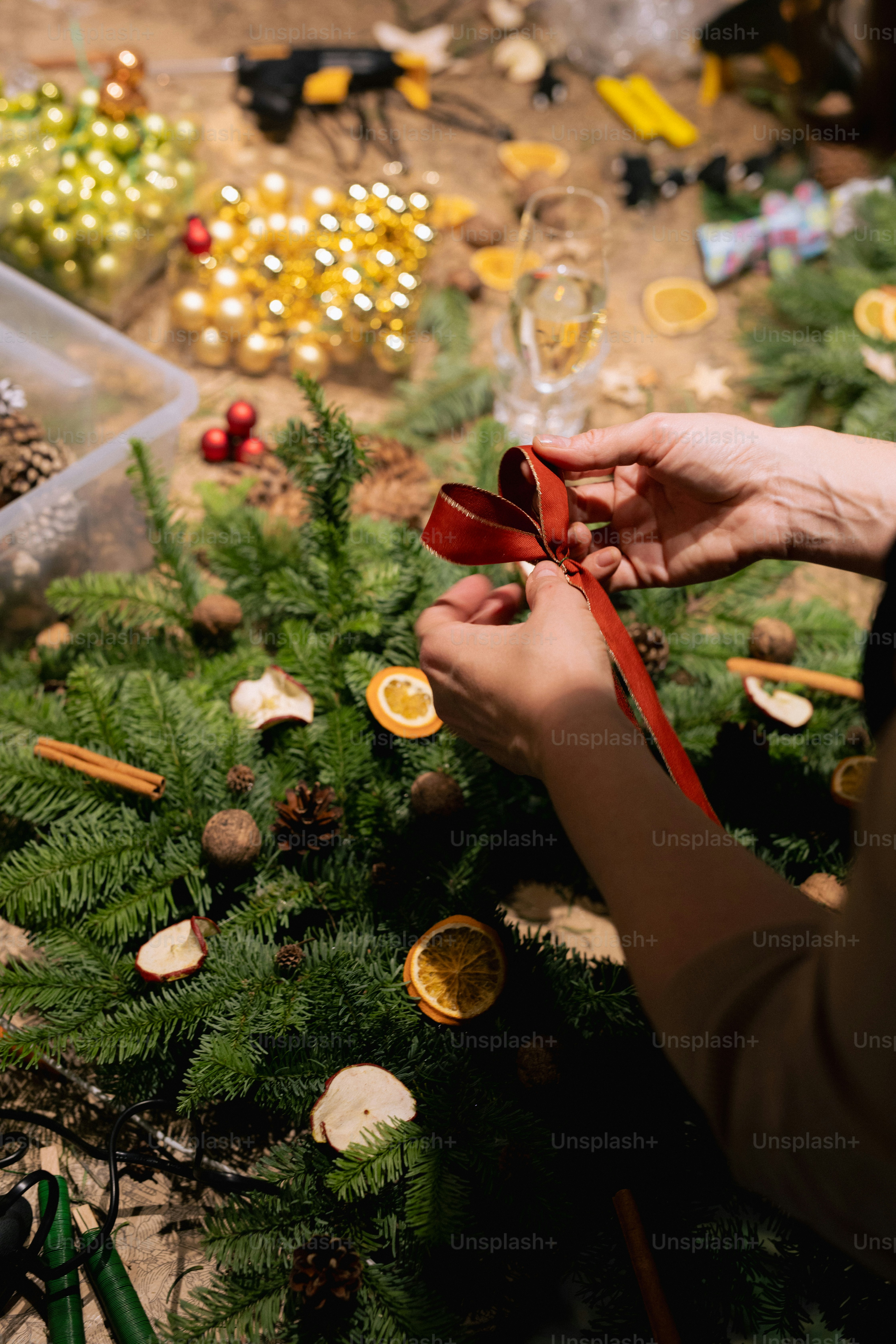 Hands decorating a christmas wreath with a red ribbon.