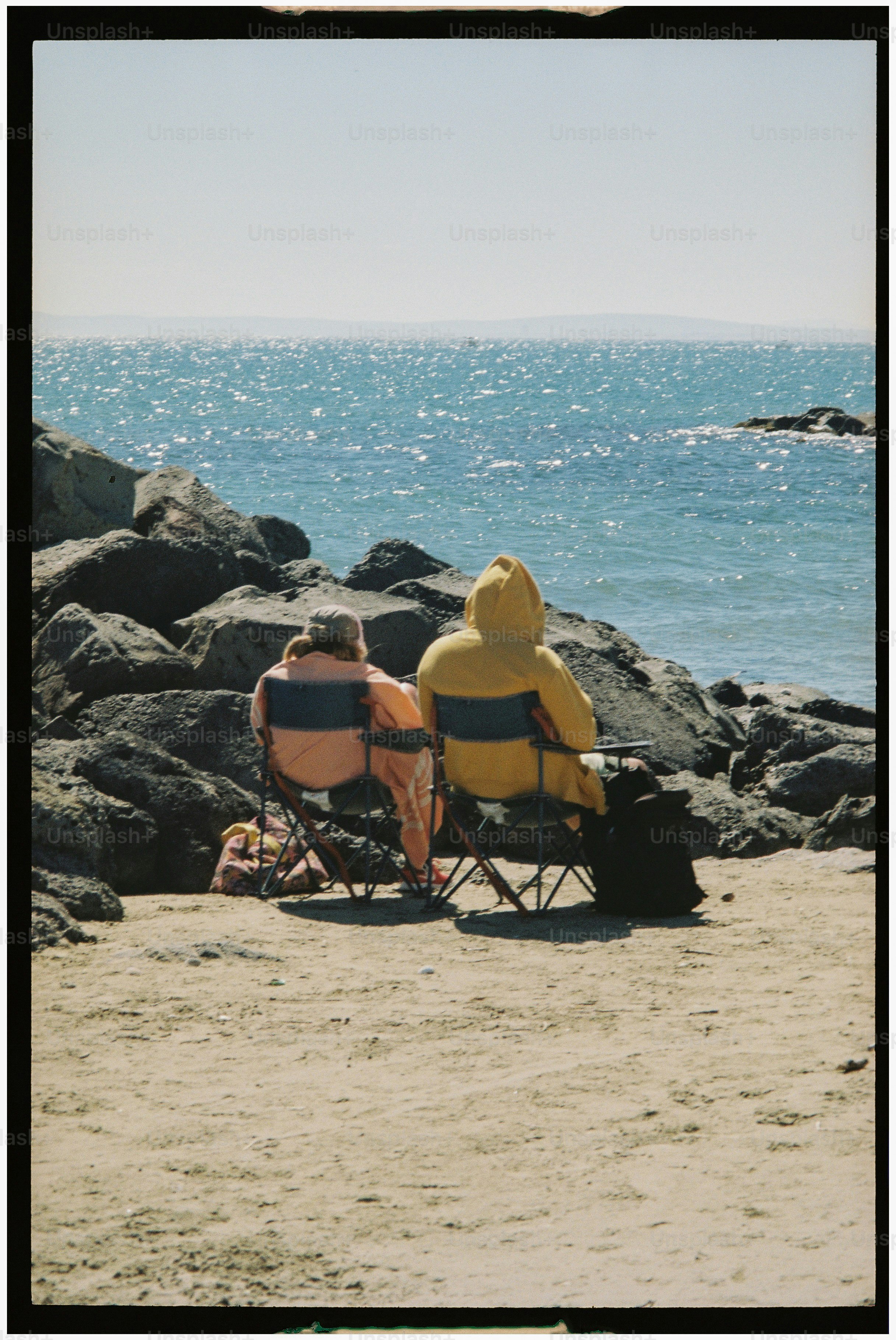 Two people sit in chairs by the ocean.