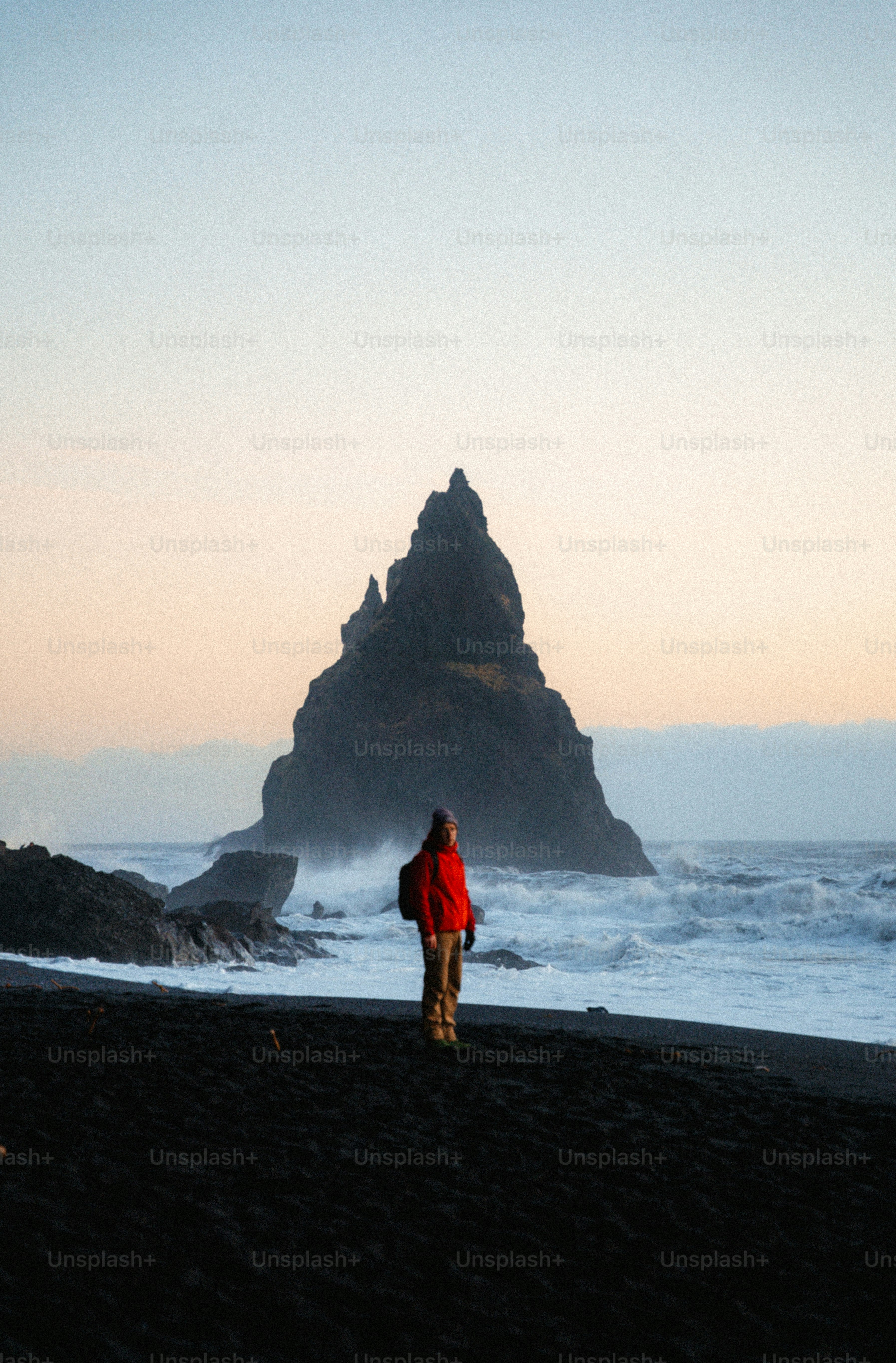 Person standing on black sand beach facing rock formation