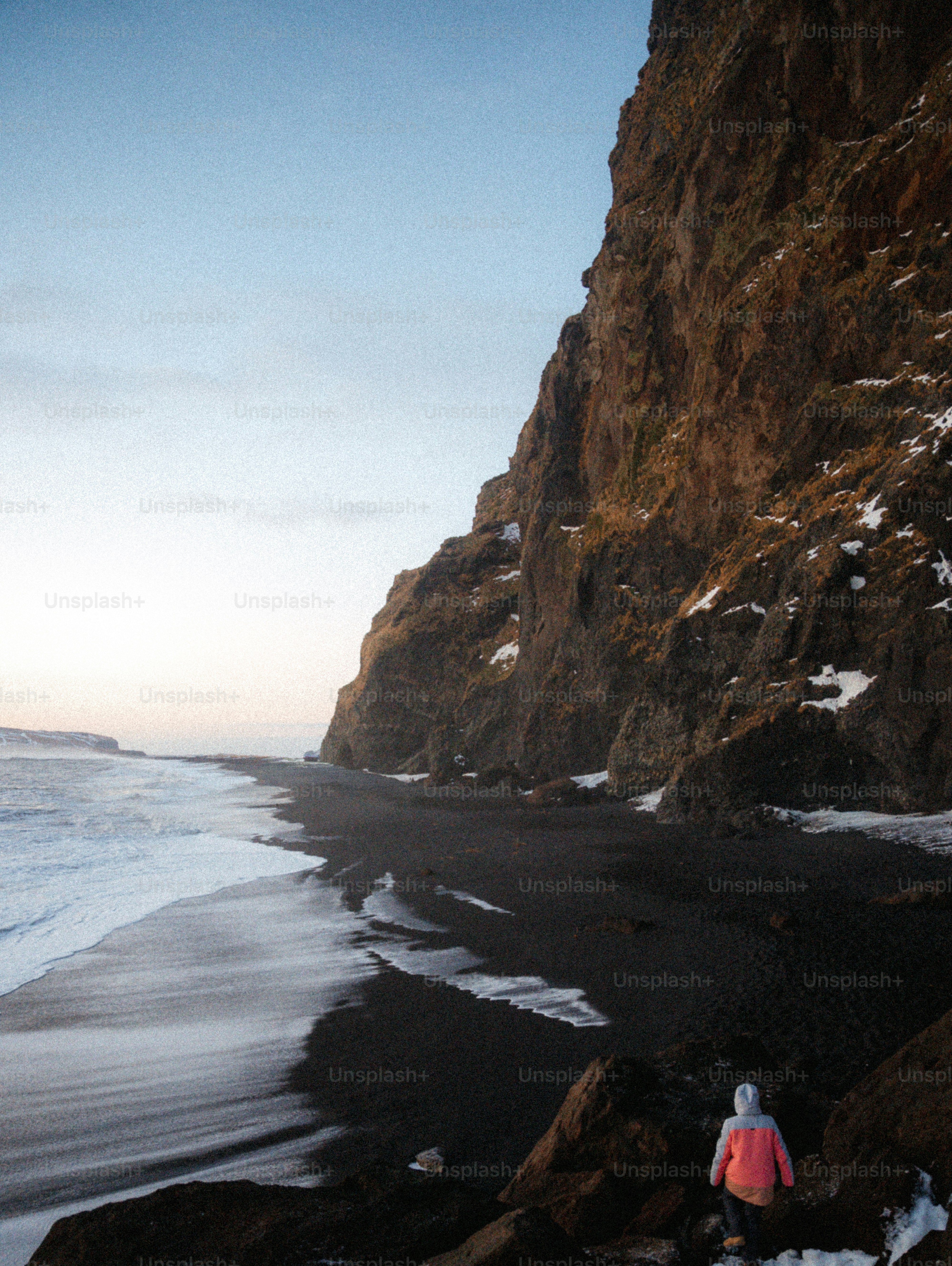 Person on black sand beach with large cliff