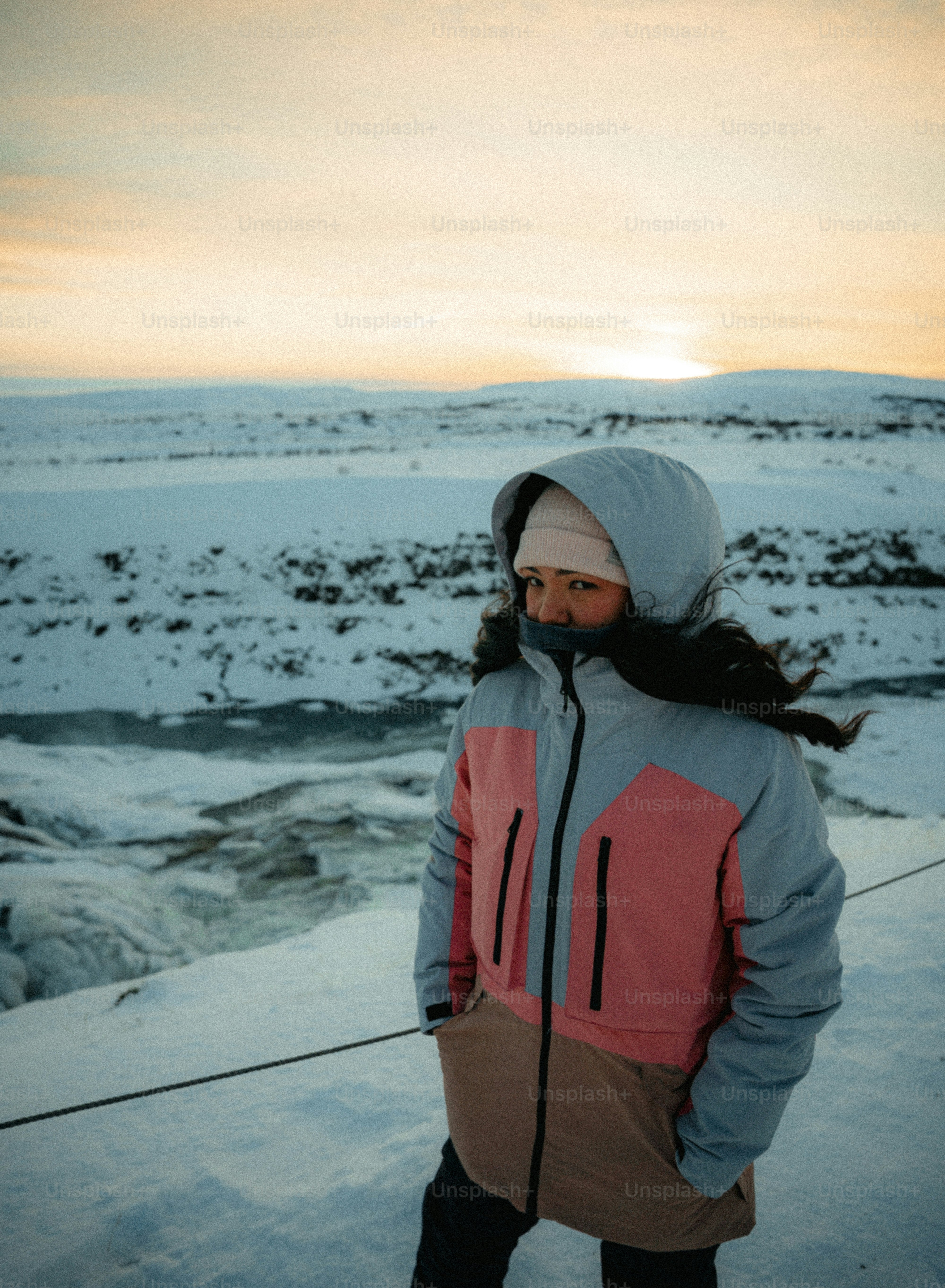 Woman in winter jacket by snowy waterfall at sunset