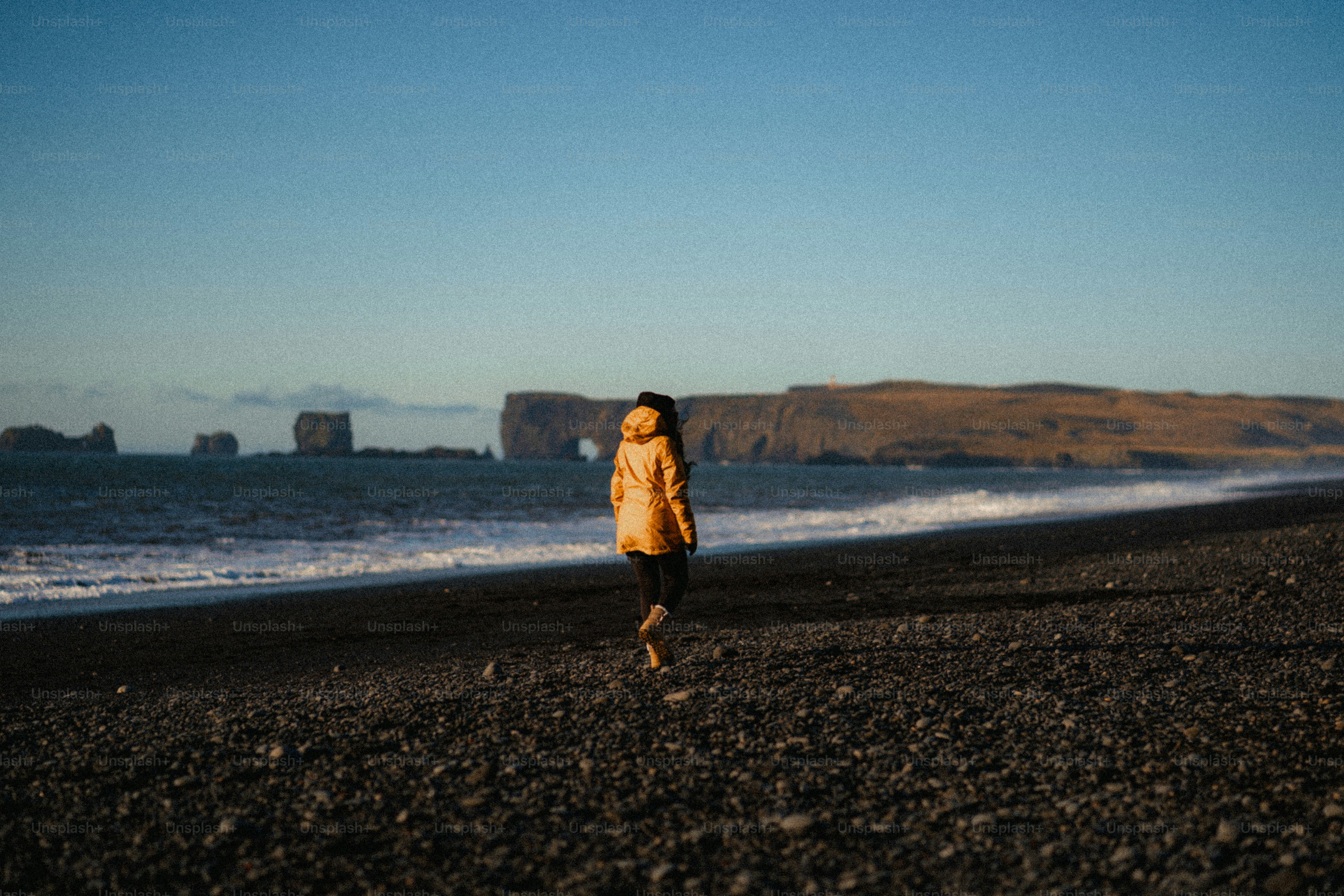 Person walks on a black sand beach towards ocean
