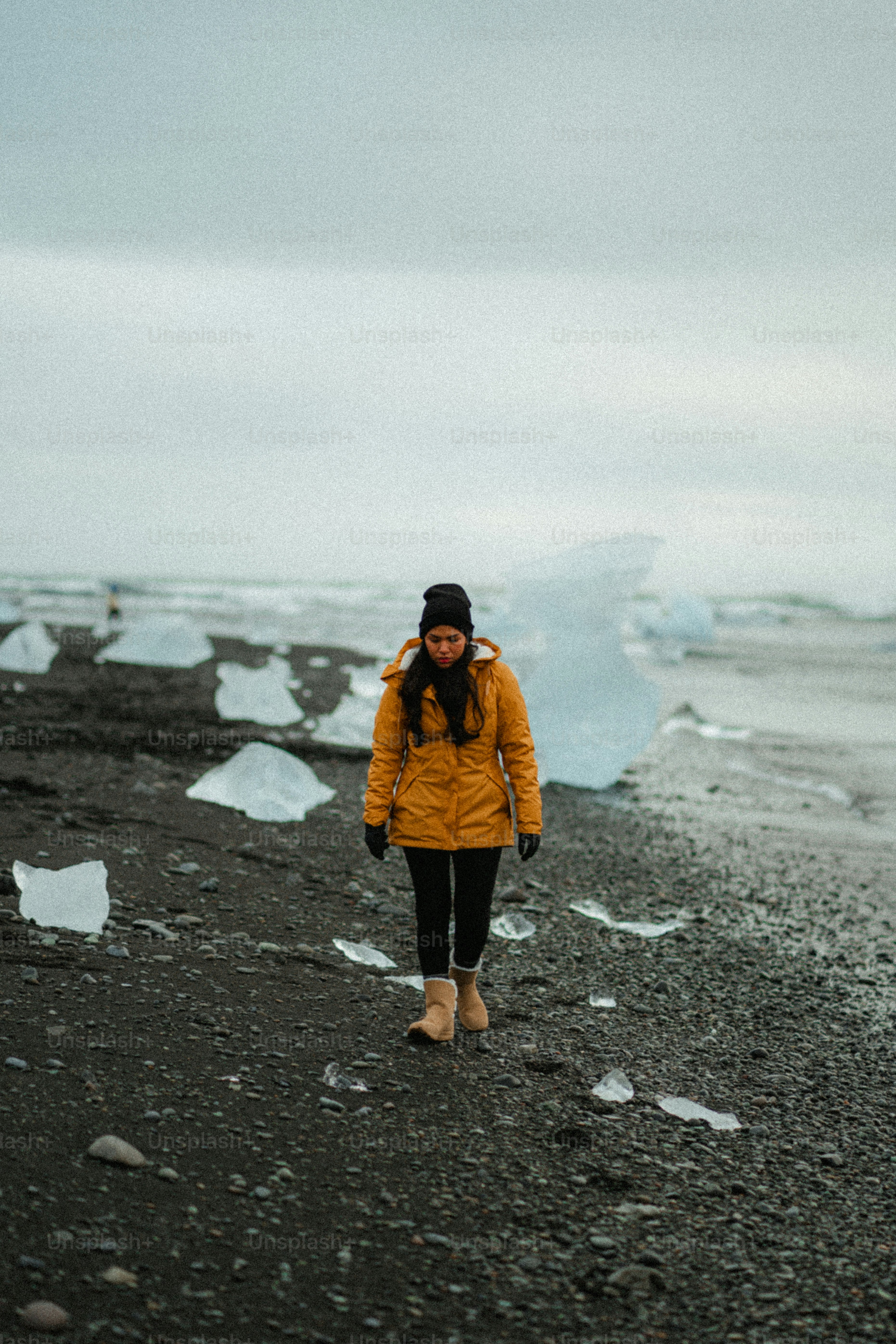 Woman walking on a black sand beach with ice chunks