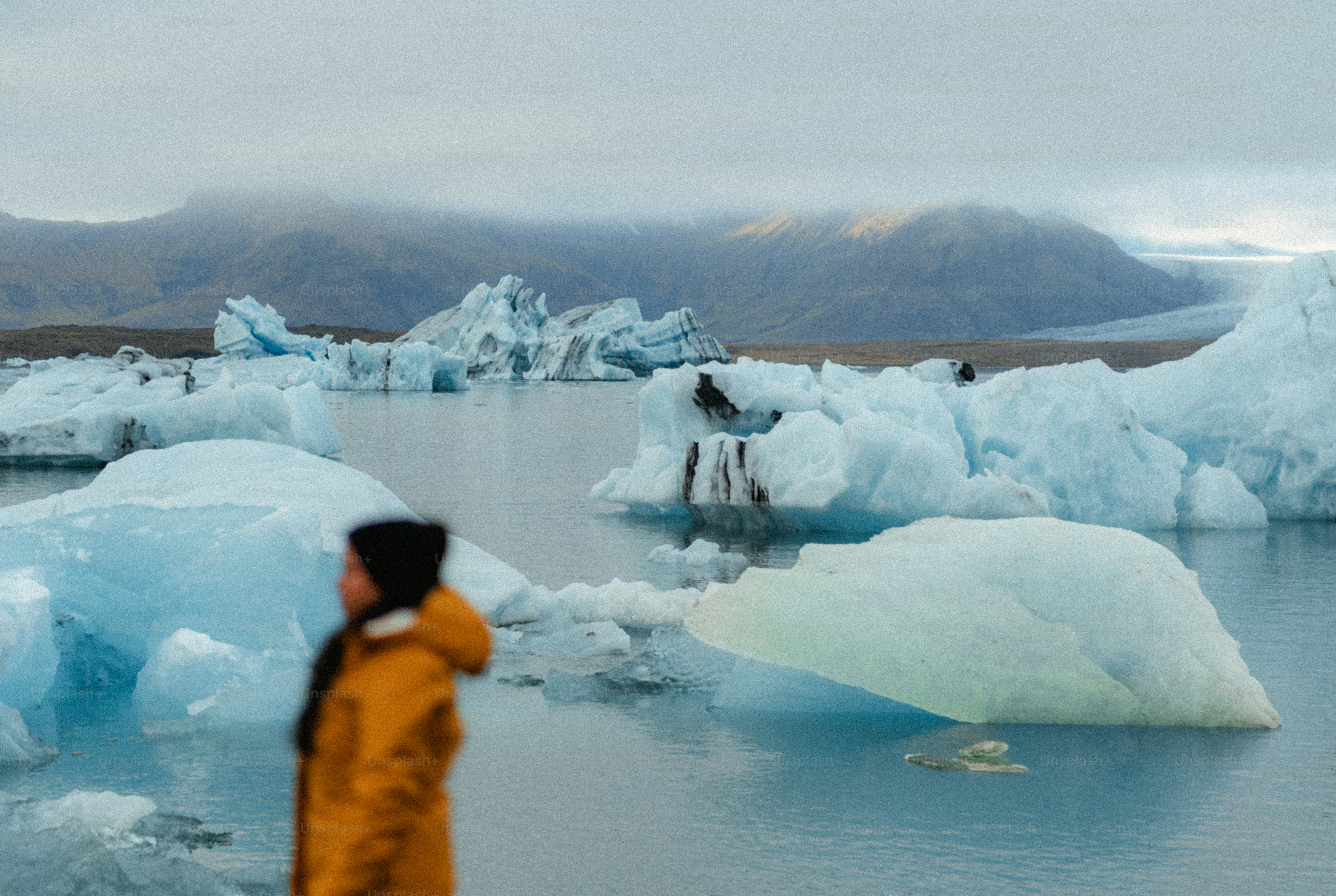 Person in yellow jacket observes icebergs in glacial lagoon
