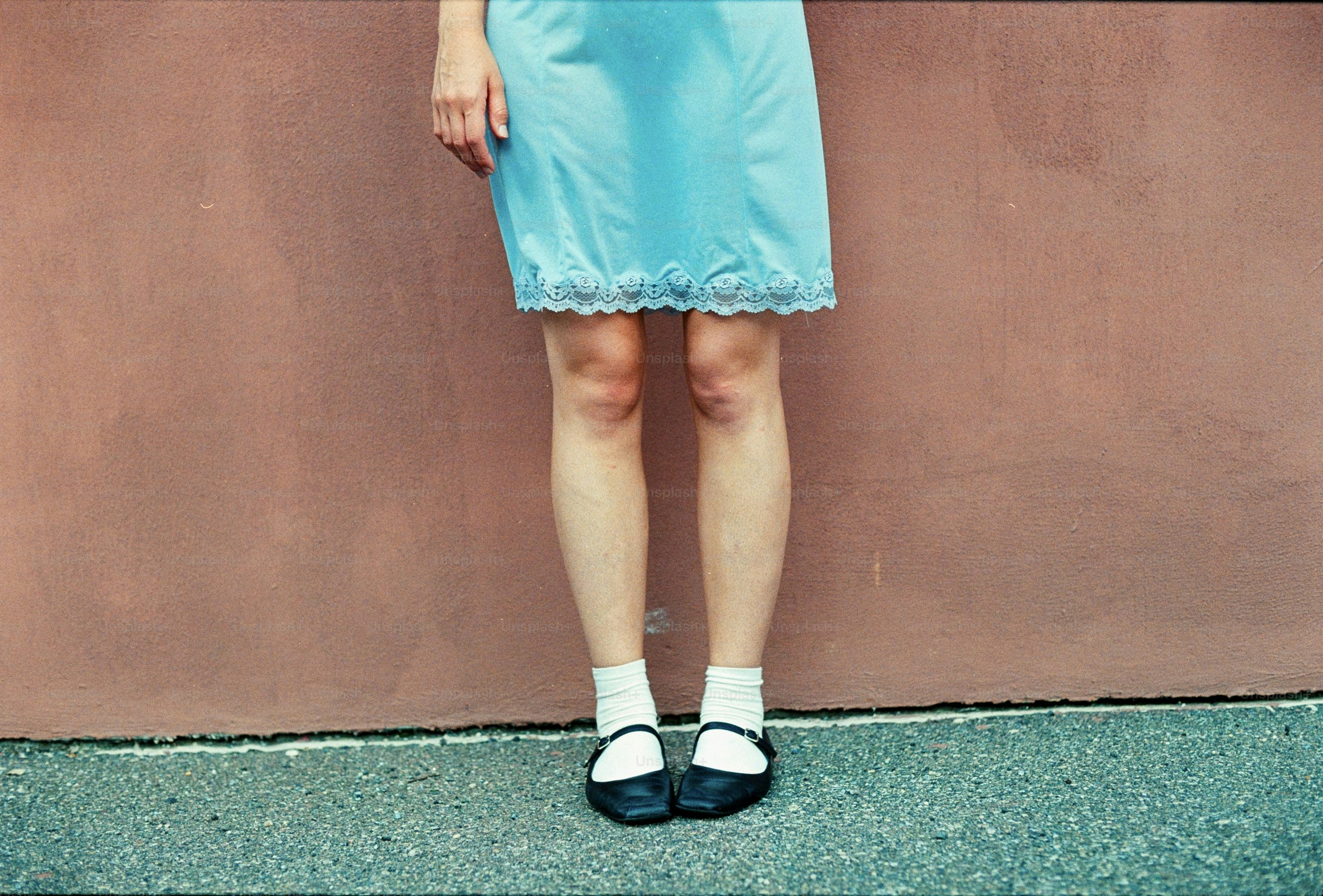 Woman in blue slip and white socks stands against wall