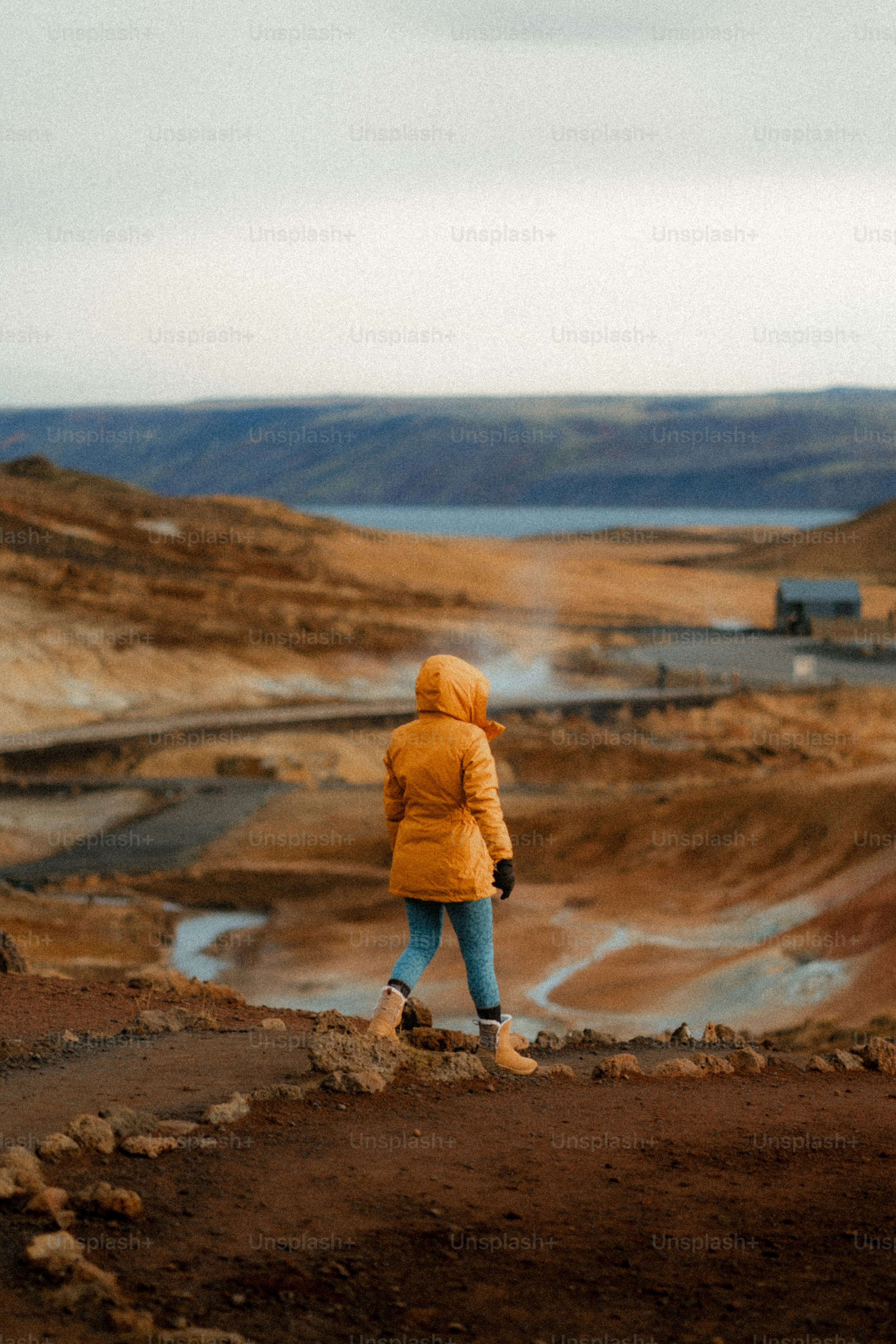 Woman in yellow jacket walks through geothermal landscape.