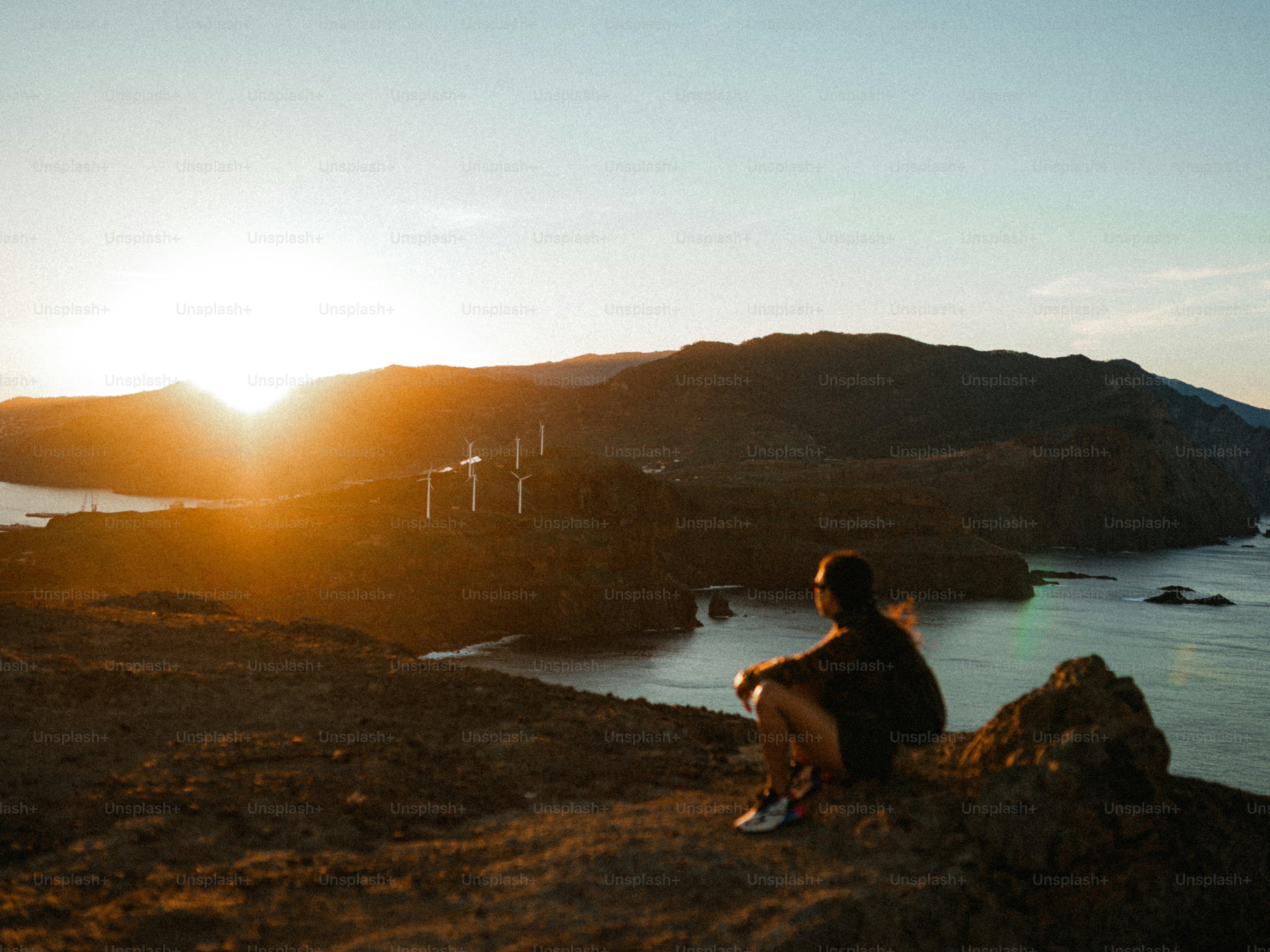 Person watches sunset over hills and ocean.