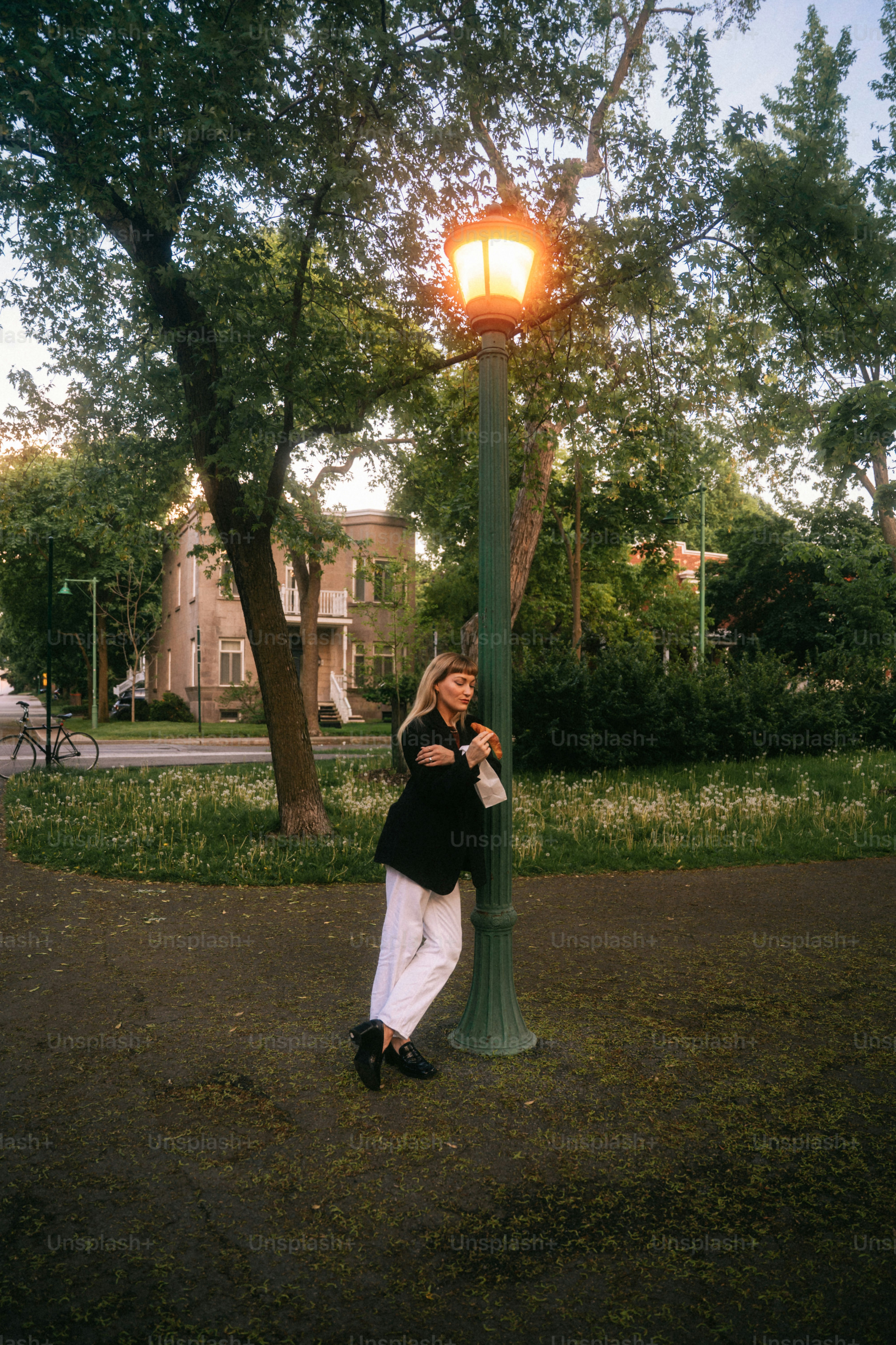 Woman leaning on a lamppost in a park.