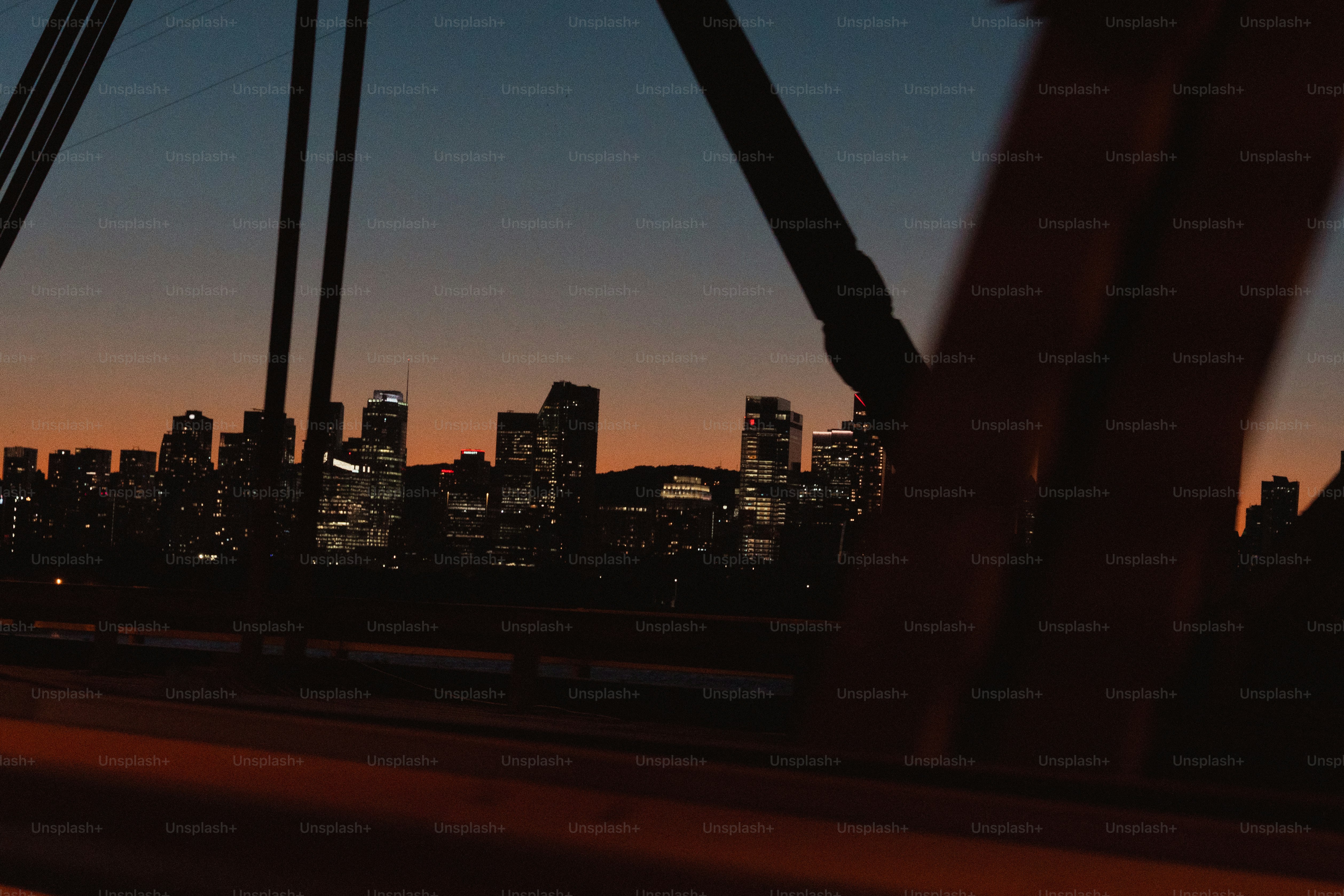 Horizonte da cidade iluminado ao entardecer com estrutura de ponte em primeiro plano