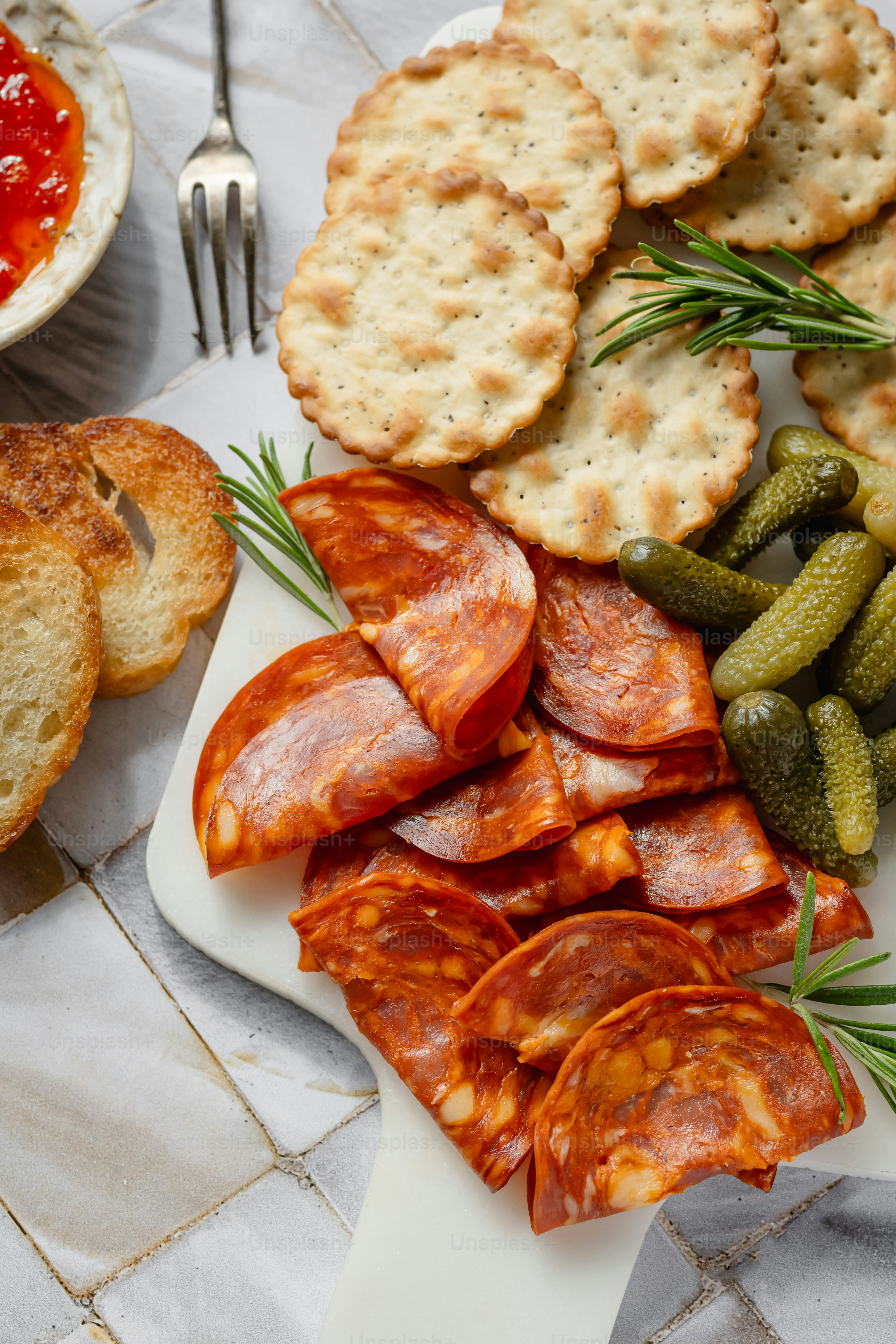 Chorizo, Cracker, Gurken und Brot auf einer Platte.