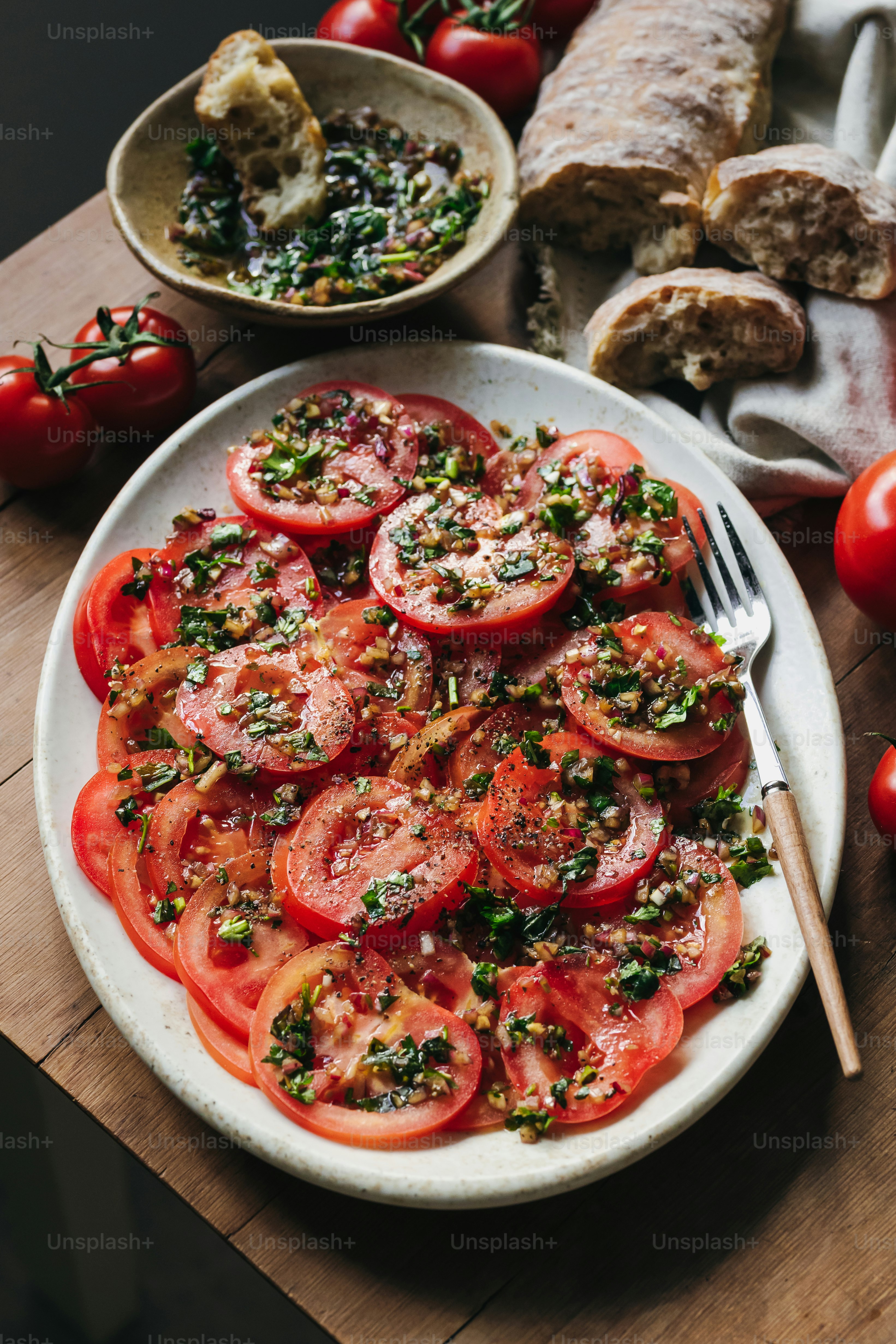 Tomatenscheiben mit Kräutern und Brot auf einem Tisch