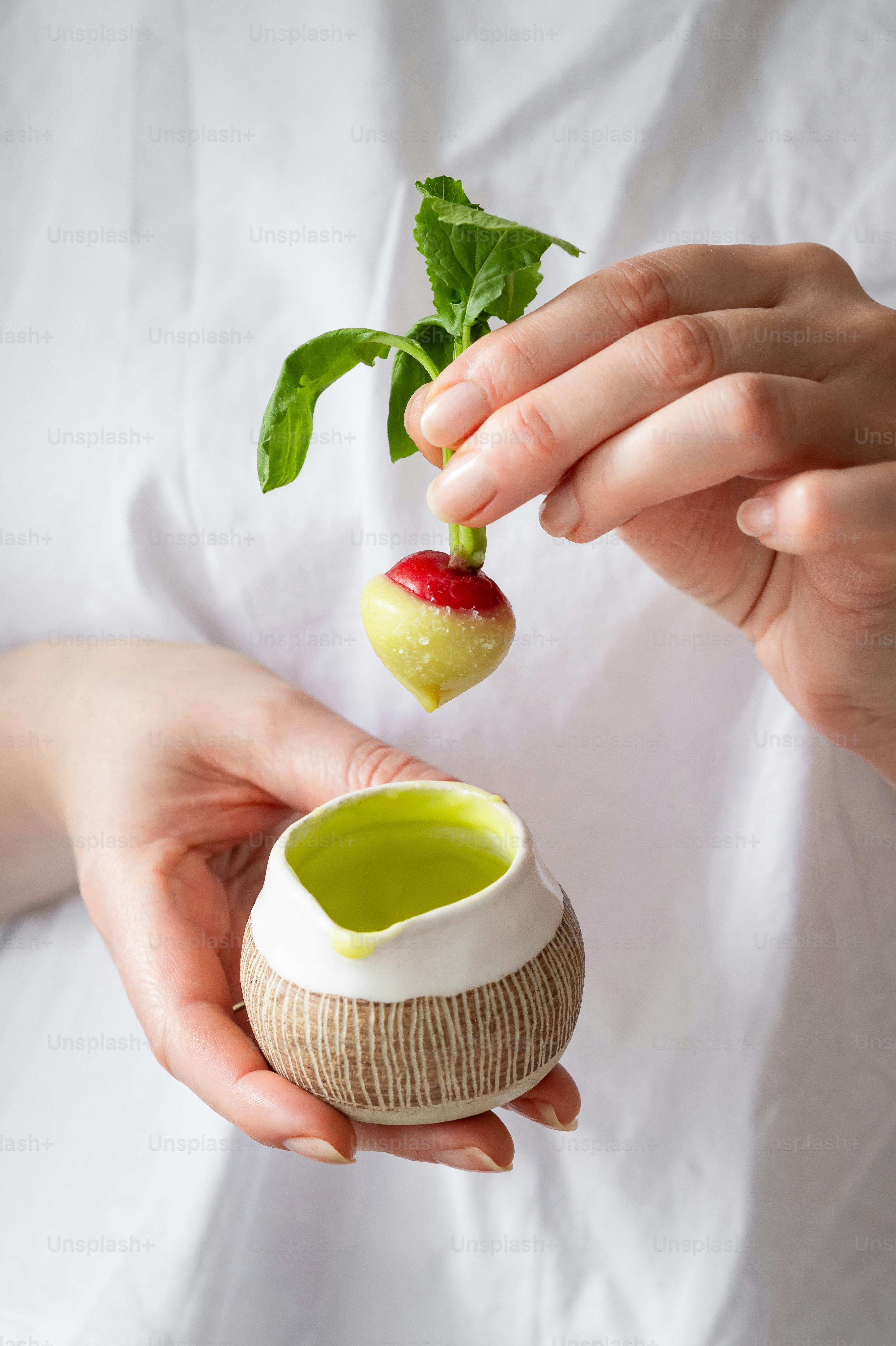 Die Hände halten Rettich über einem kleinen Keramikkrug