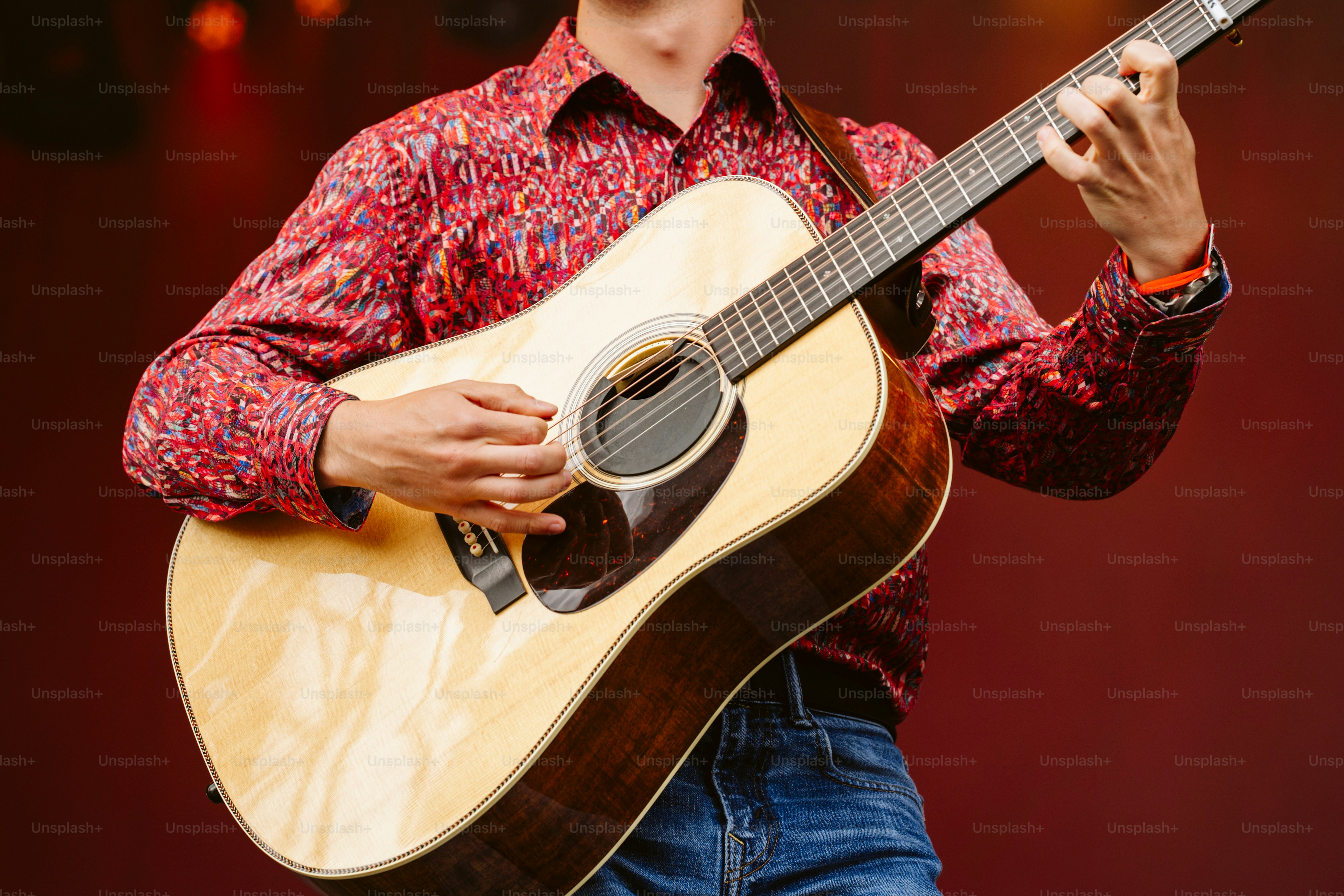 Un homme en chemise à motifs joue de la guitare acoustique sur scène