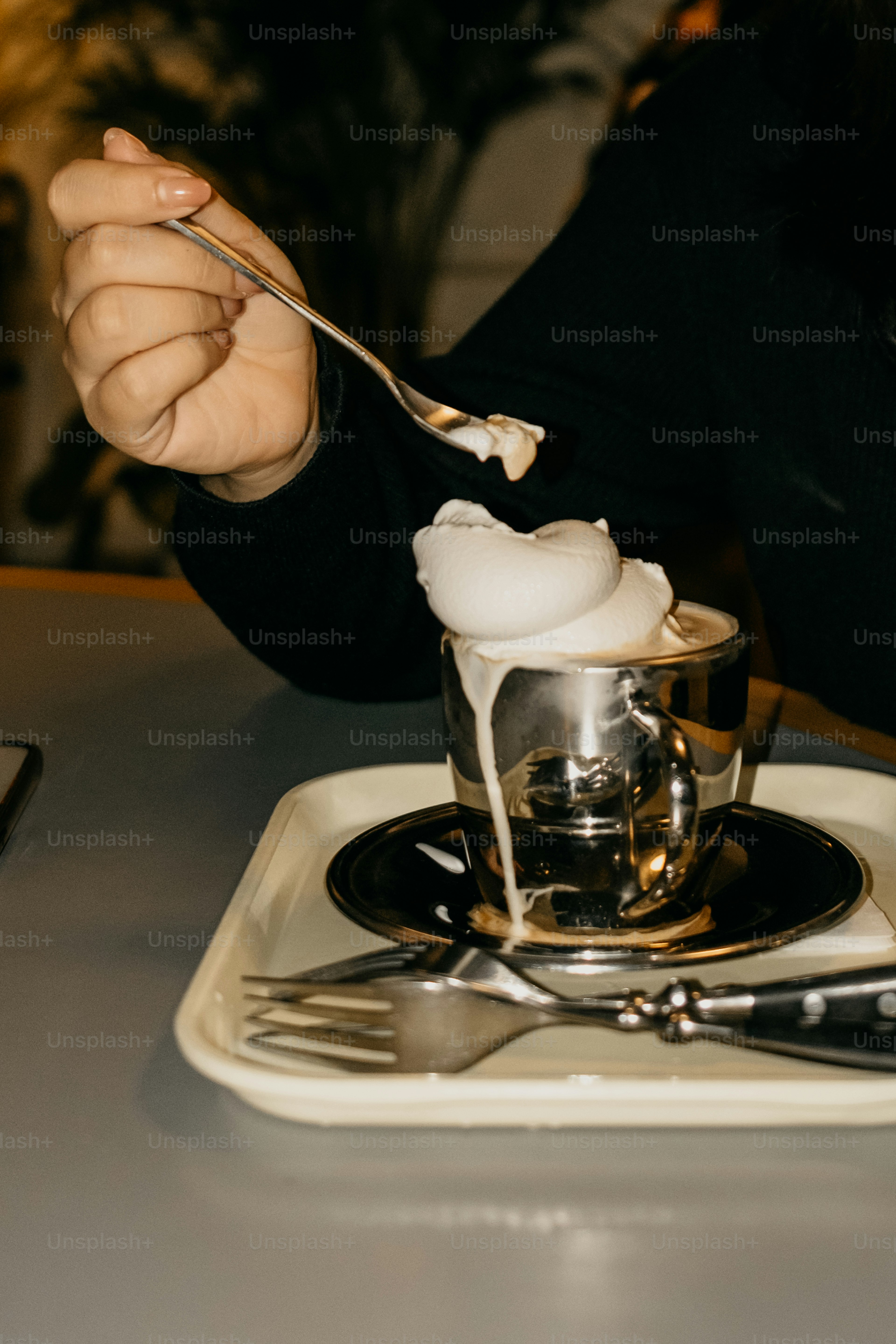 Eine Hand schöpft schaumige Sahne aus einem metallischen Becher.