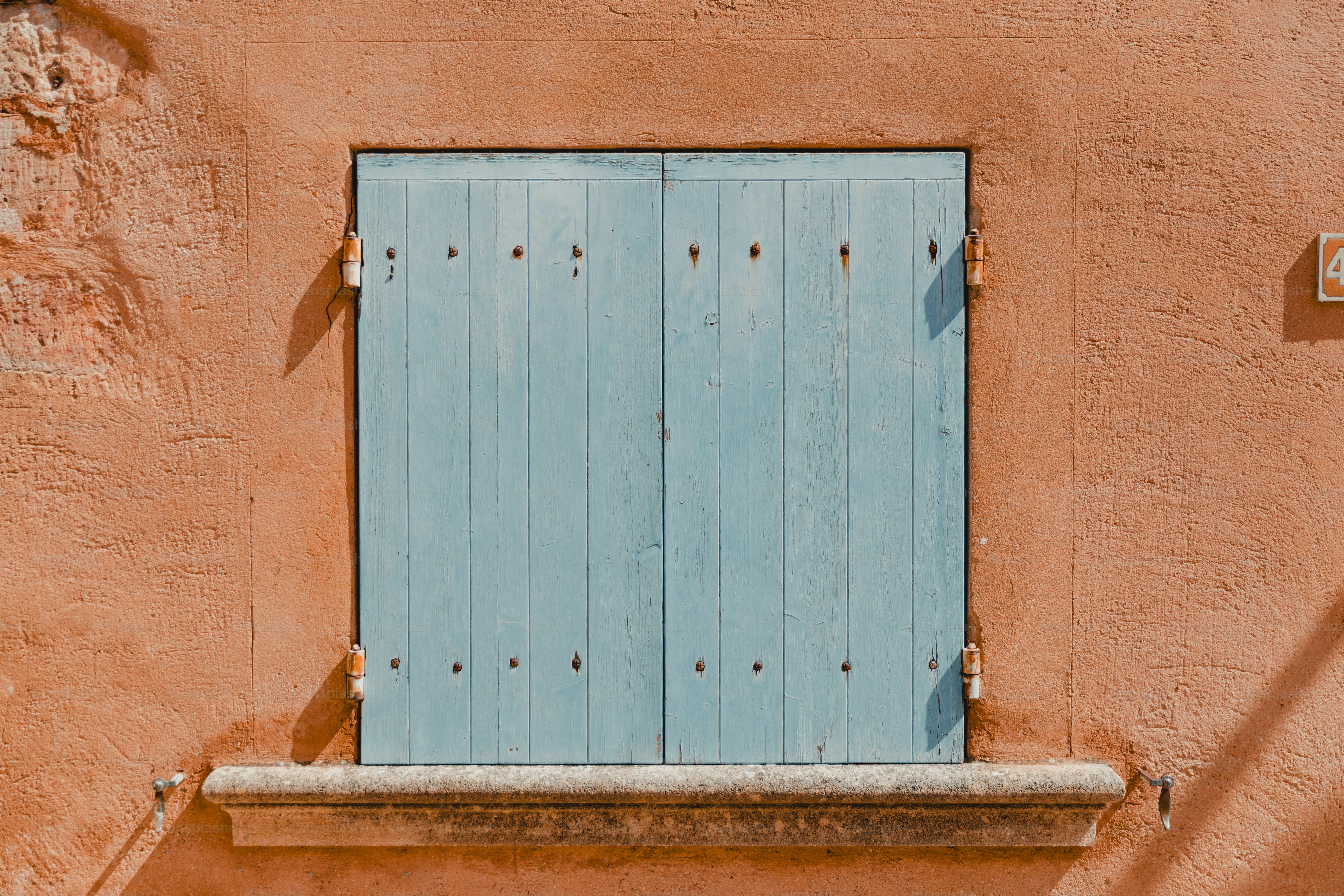 Des volets bleu clair sur un mur orange texturé.