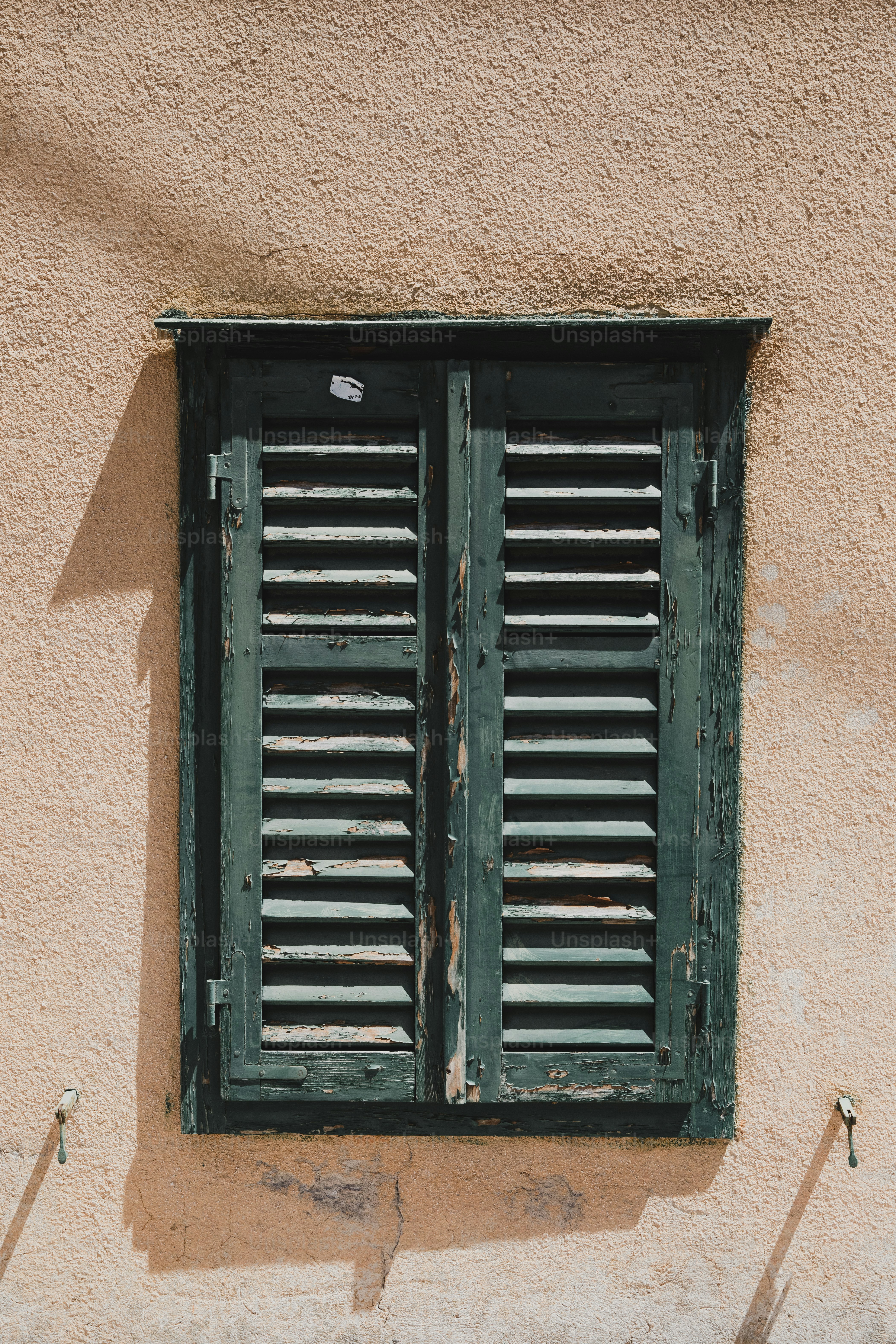 Des volets vert foncé fermés sur un mur texturé.