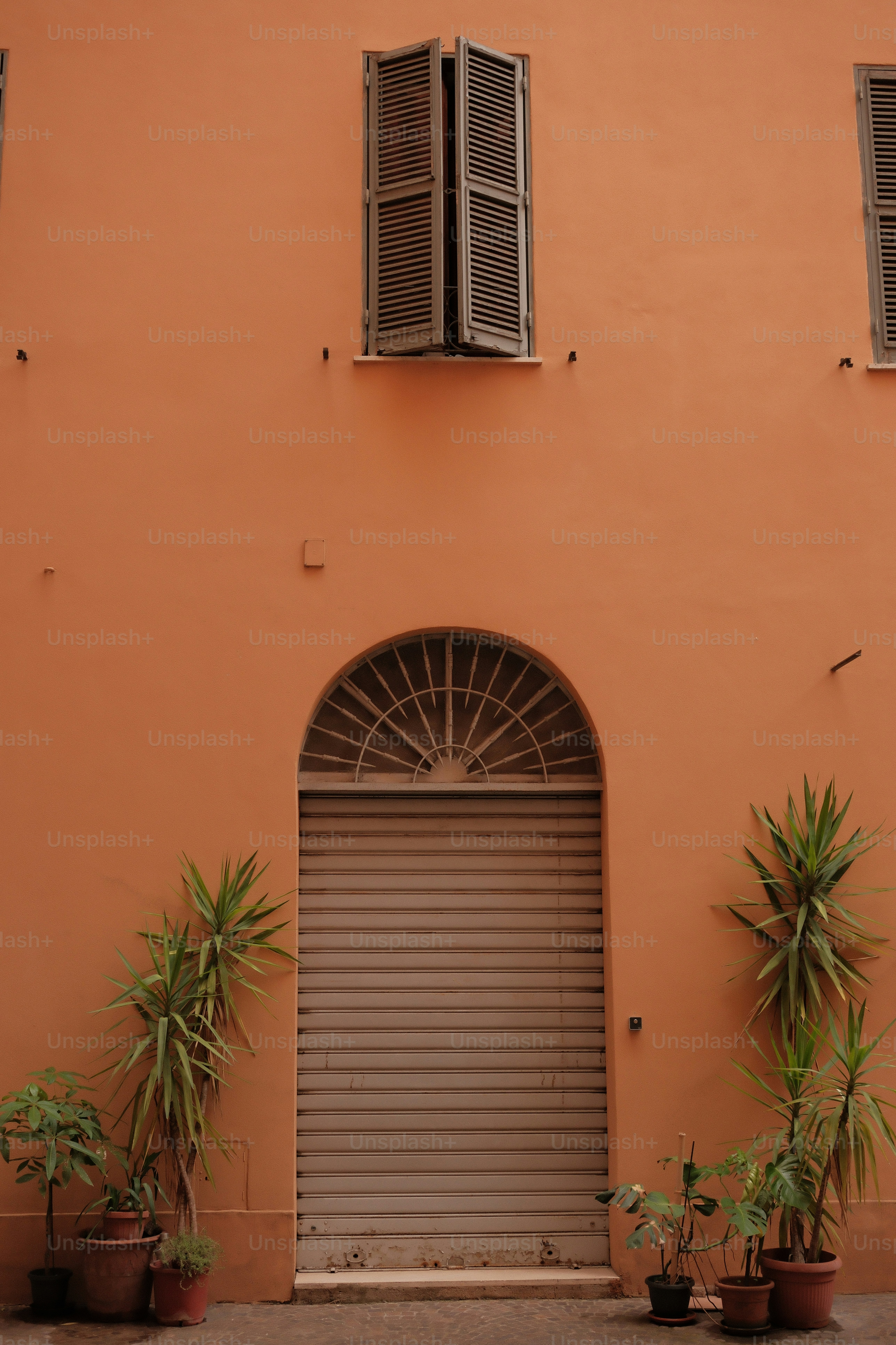 Muro naranja con puerta arqueada y plantas en maceta