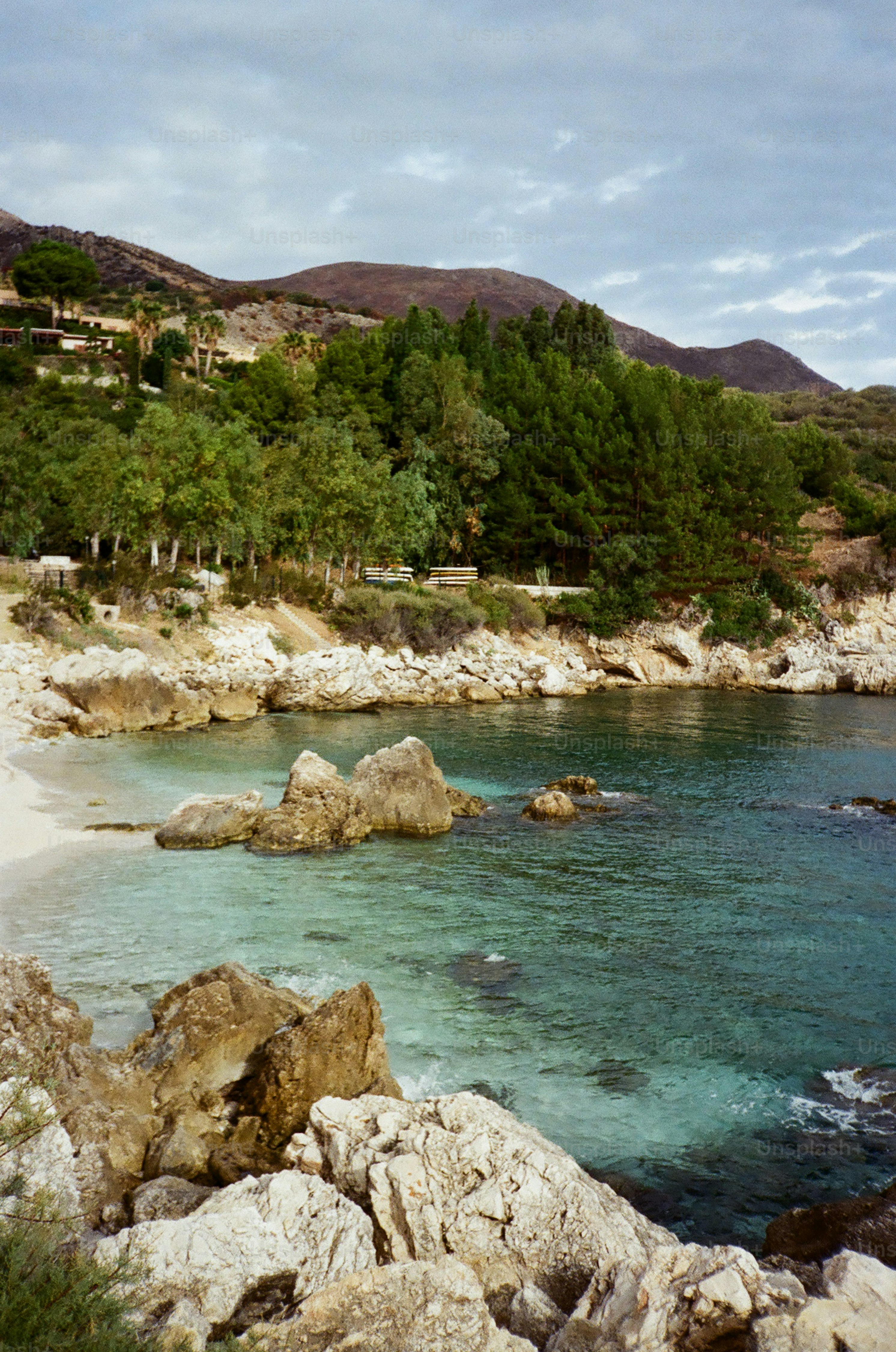 Rocky coastline with clear turquoise water and green hills.
