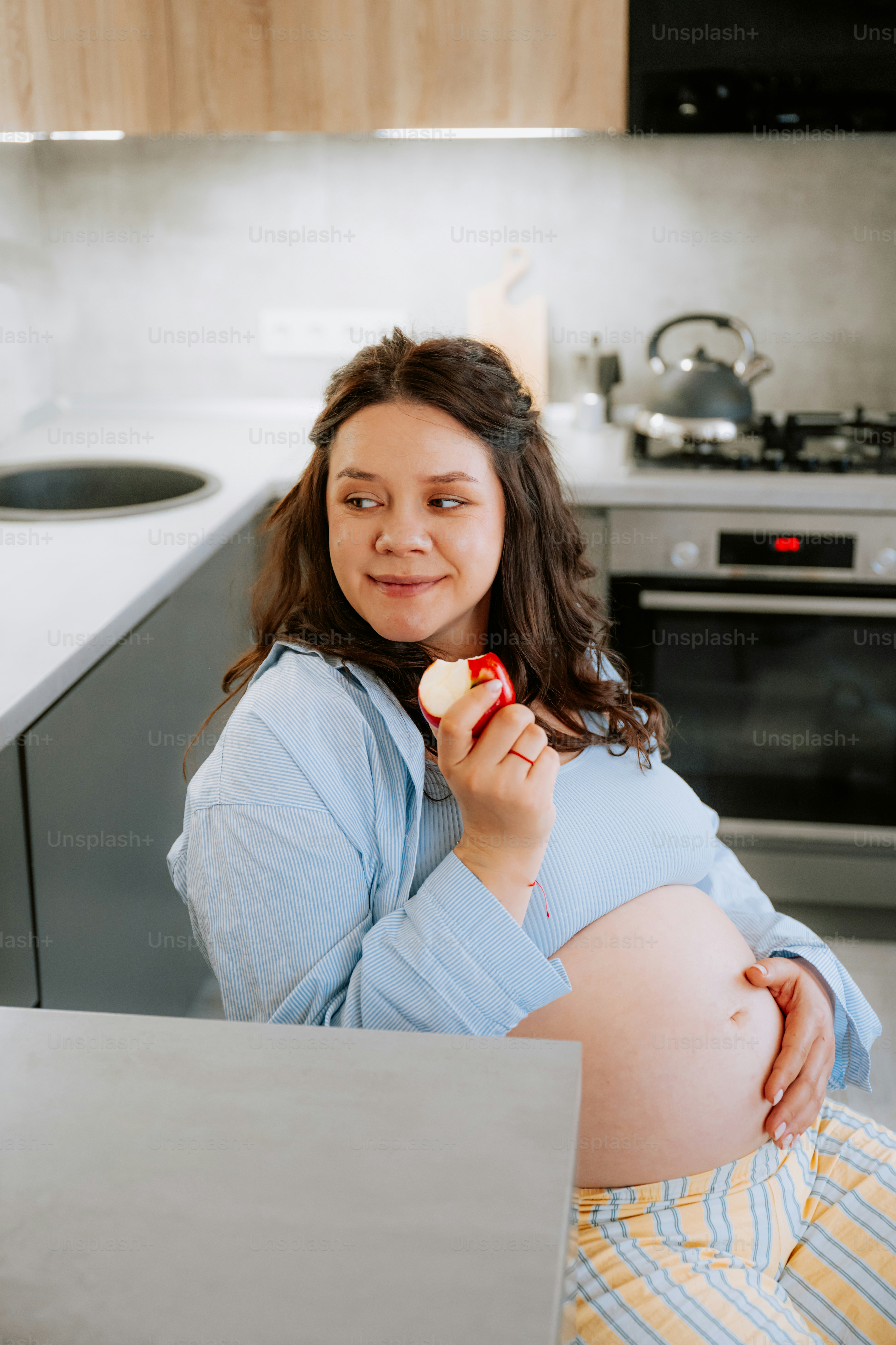 Pregnant woman eating an apple in the kitchen