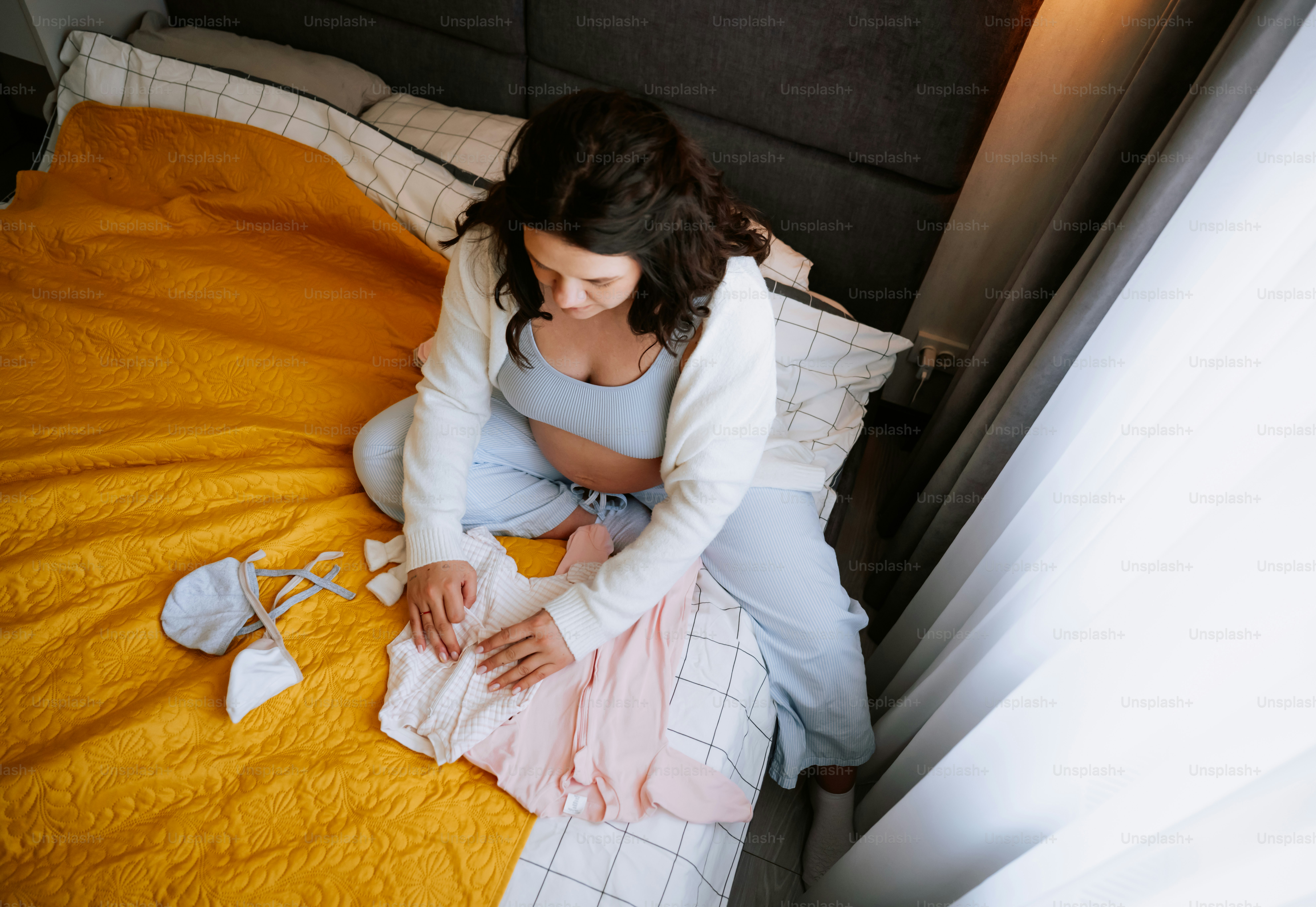 Mujer embarazada doblando ropa de bebé en una cama