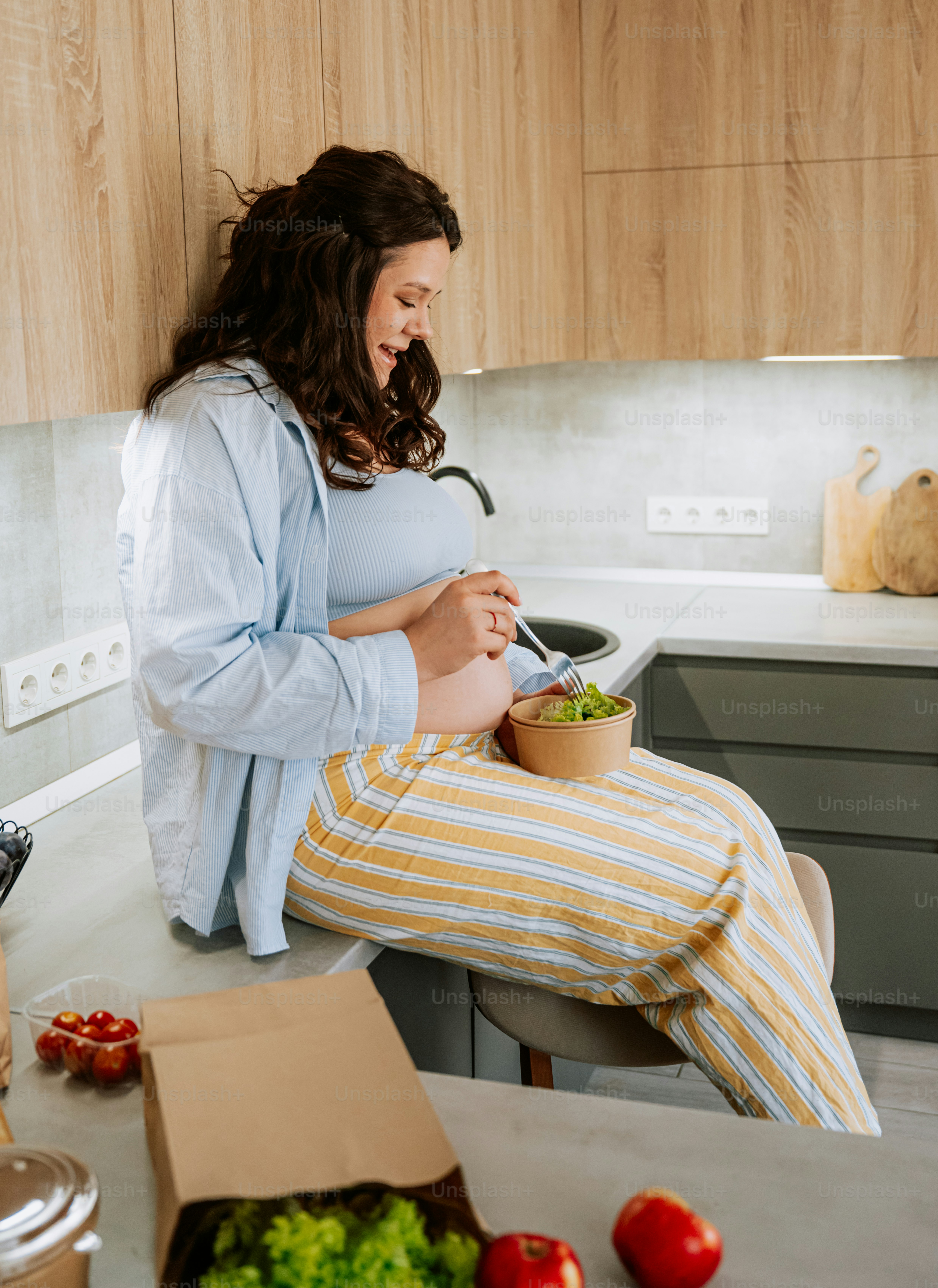 Mujer embarazada comiendo ensalada en una cocina moderna.