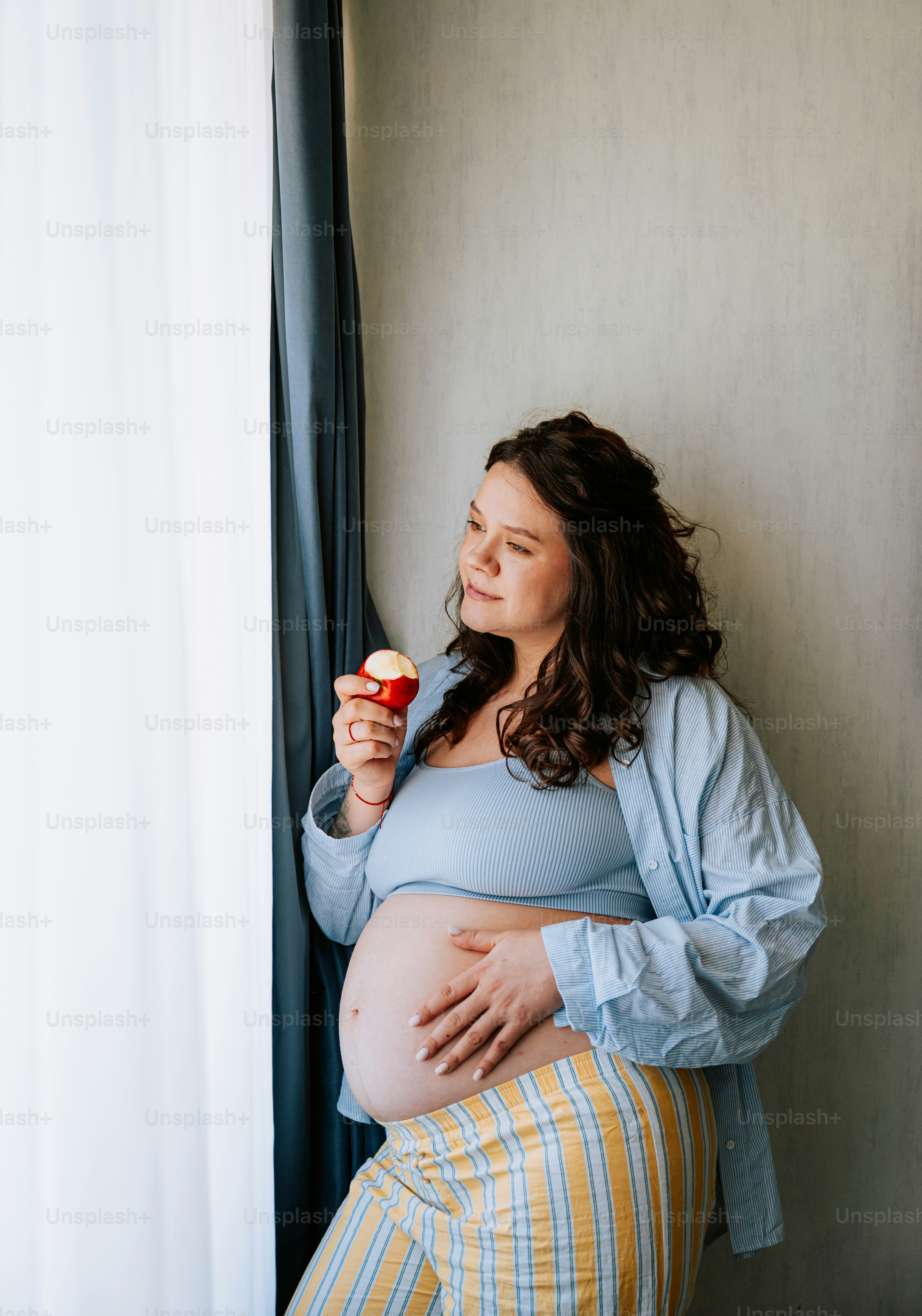 Mujer embarazada comiendo una magdalena junto a la ventana
