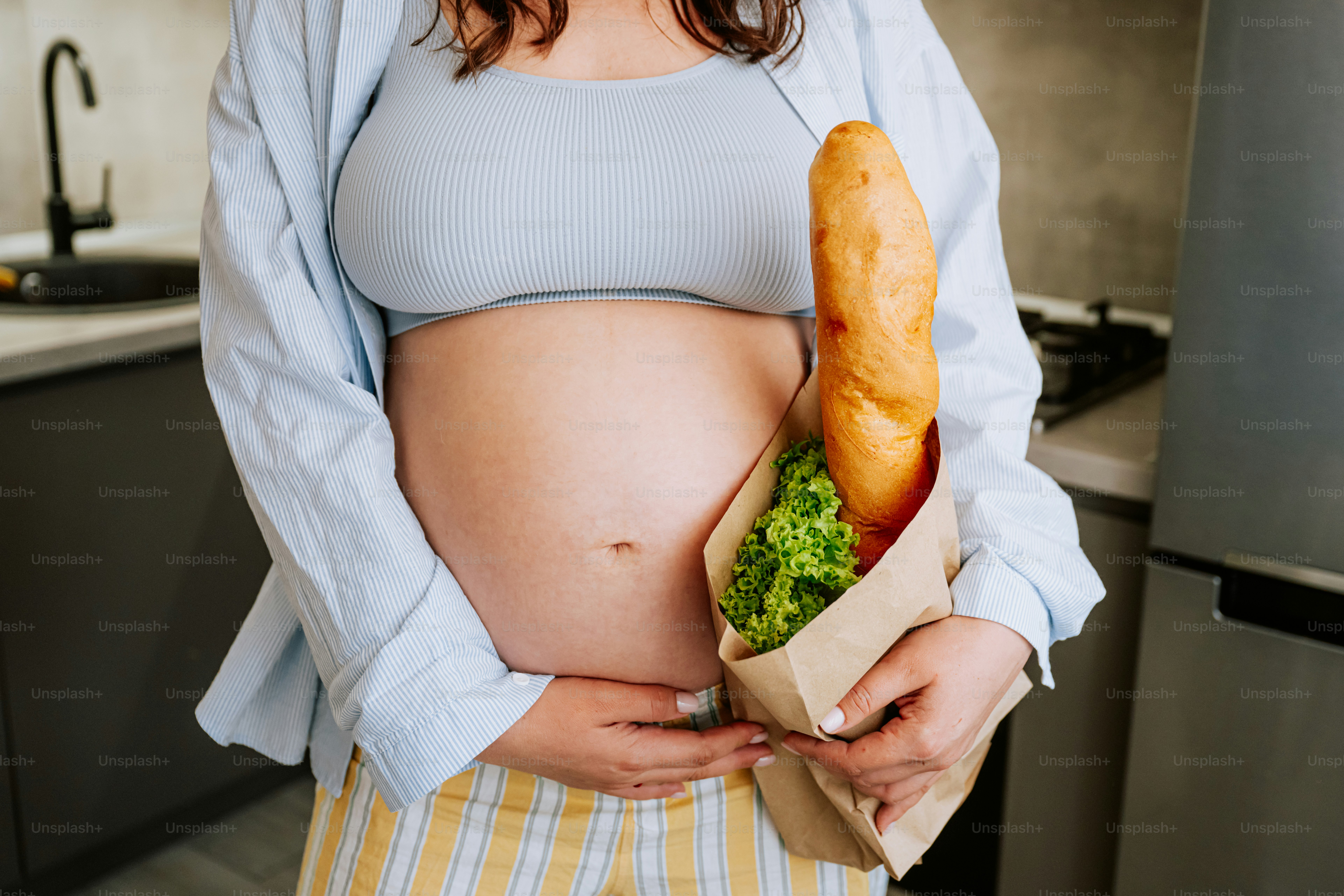 Mujer embarazada sosteniendo una baguette y lechuga