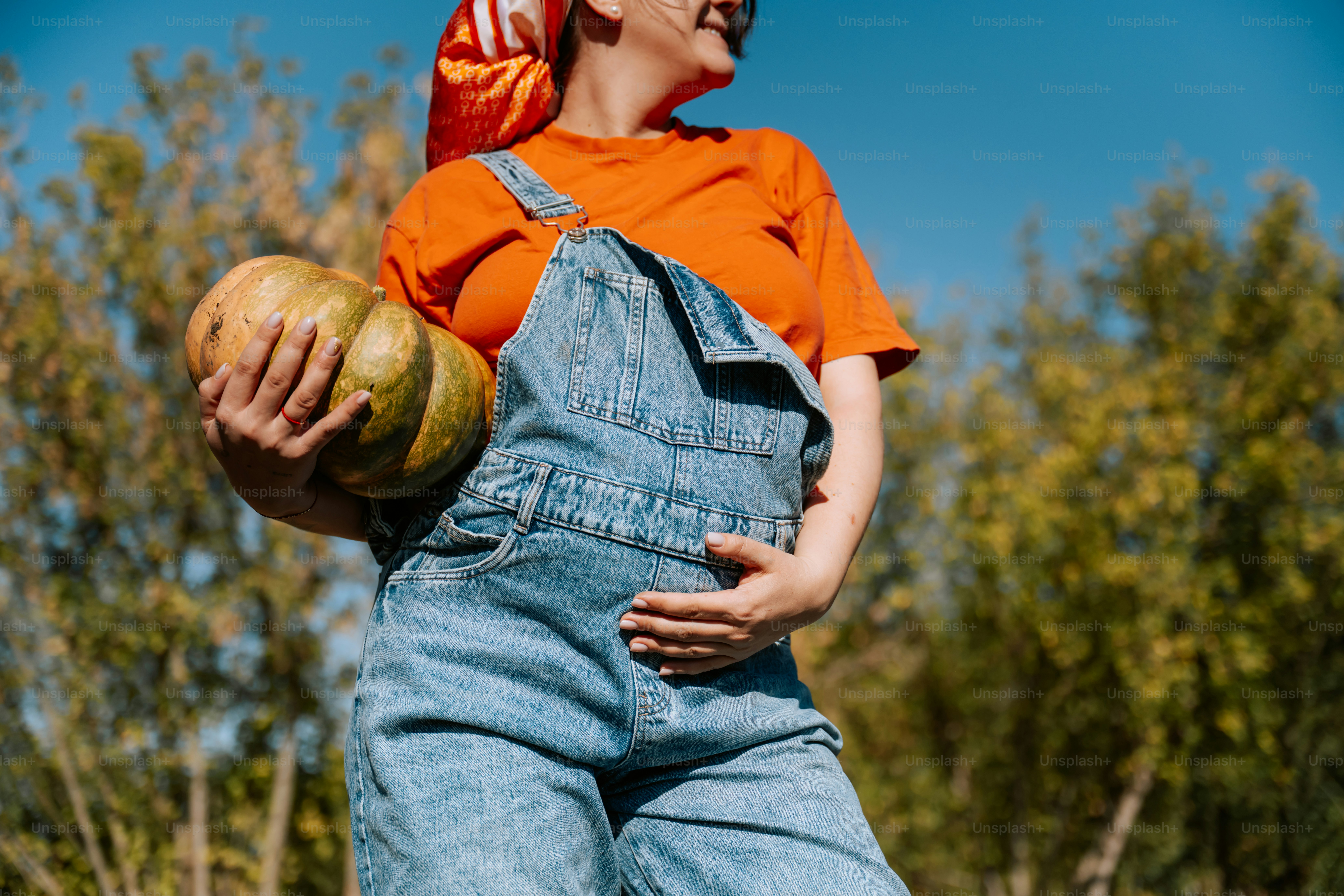 Woman in overalls holding a large pumpkin