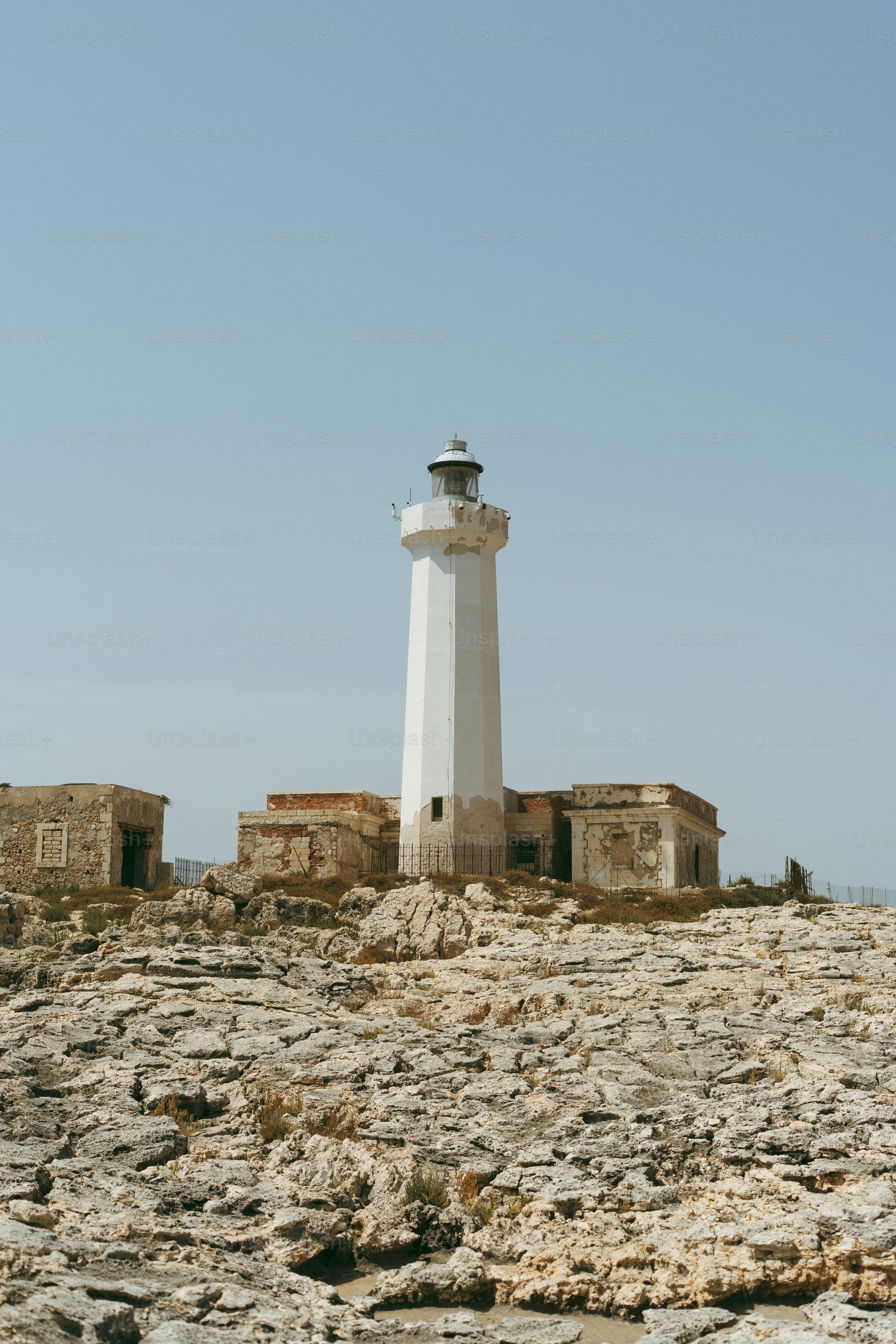 White lighthouse on a rocky shore with old buildings.